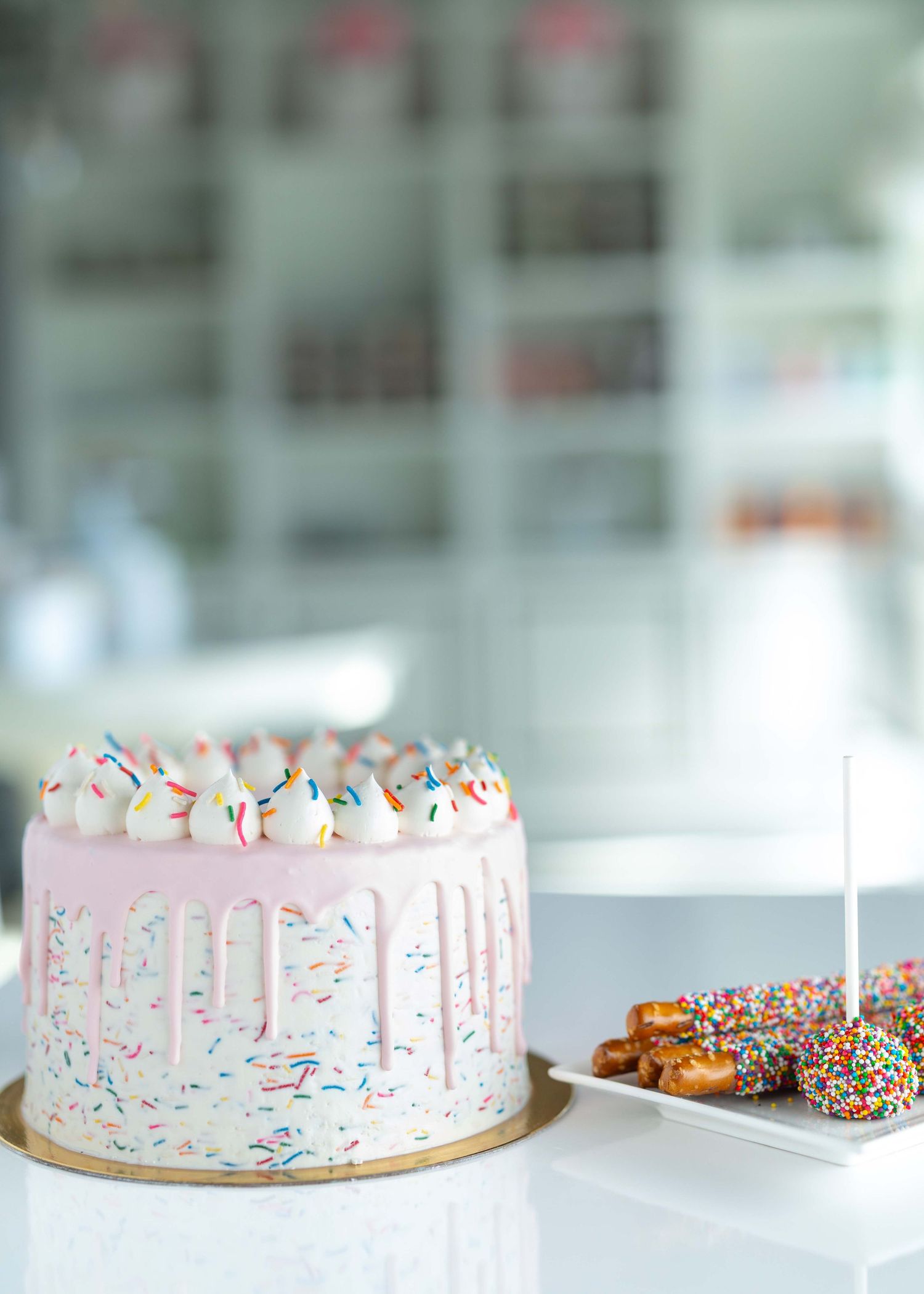 Pink drip cake decorated with rainbow sprinkles and white frosting displayed in multiple angles on a white surface.