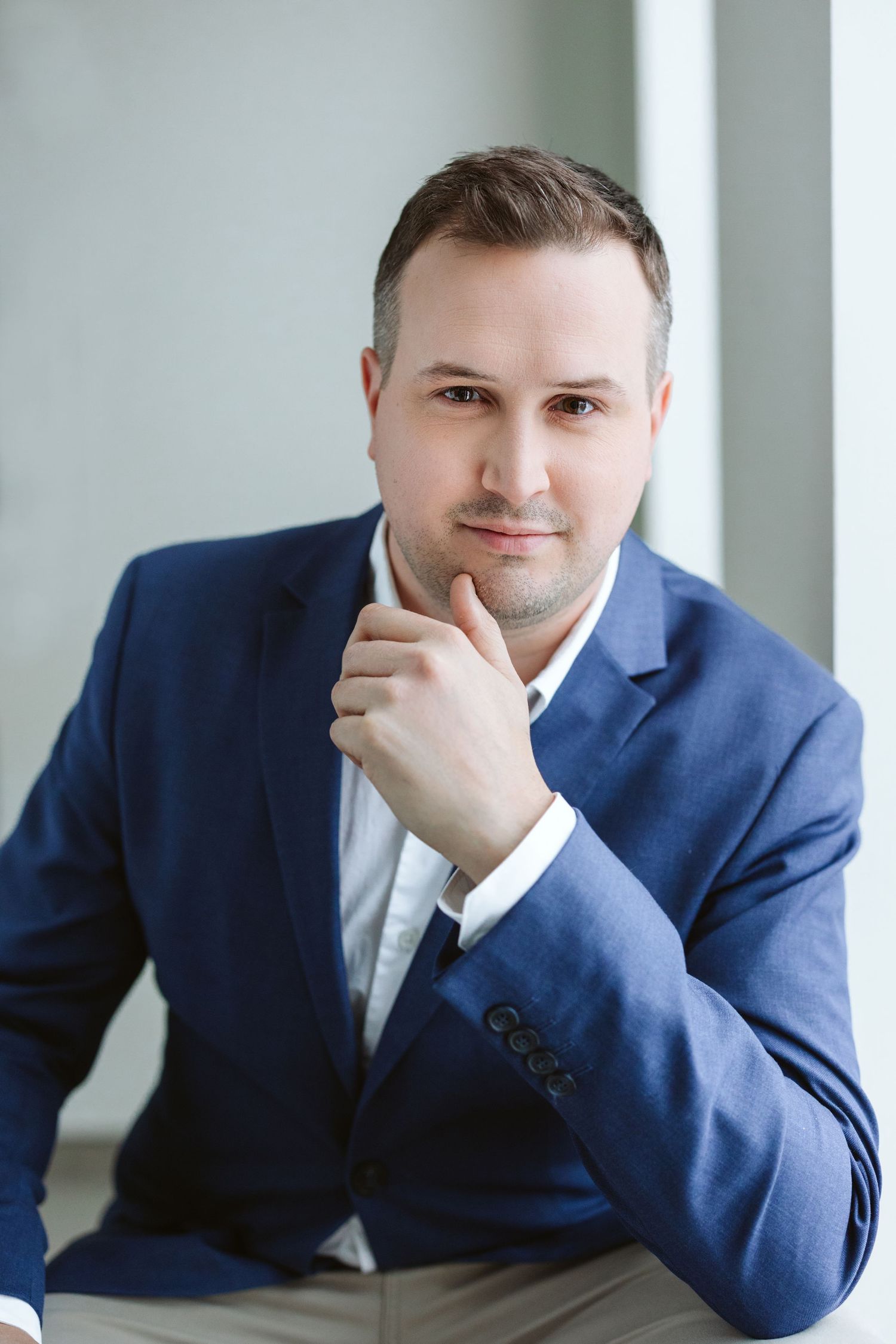 Business portraits in blue suit with contemplative poses against light backdrop.