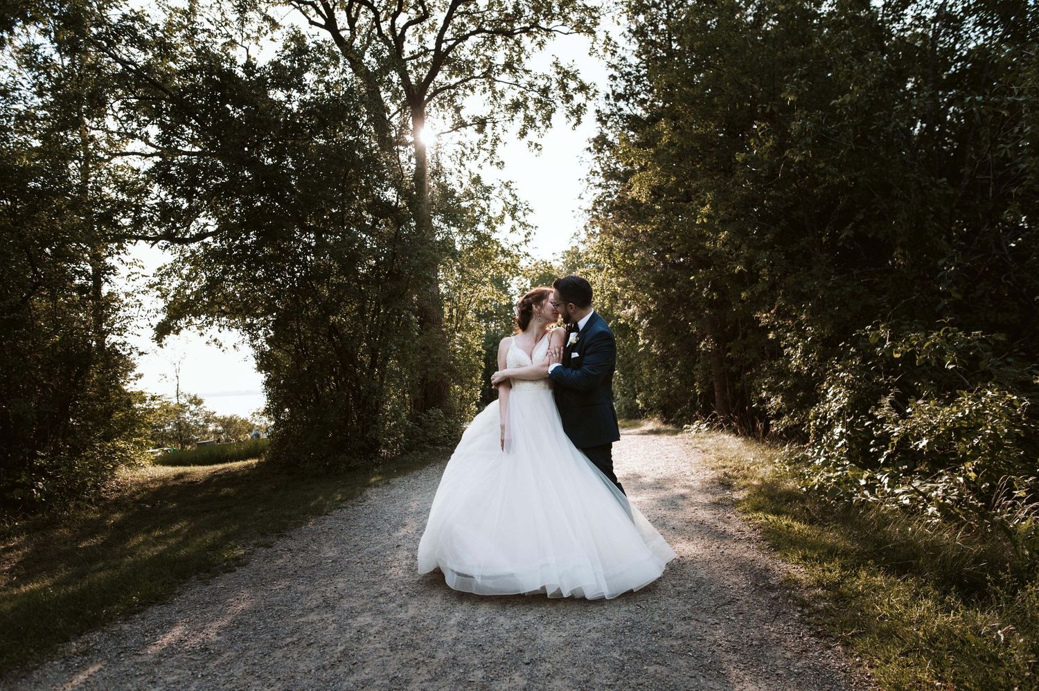 Romantic wedding portraits along tree-lined path during golden hour.