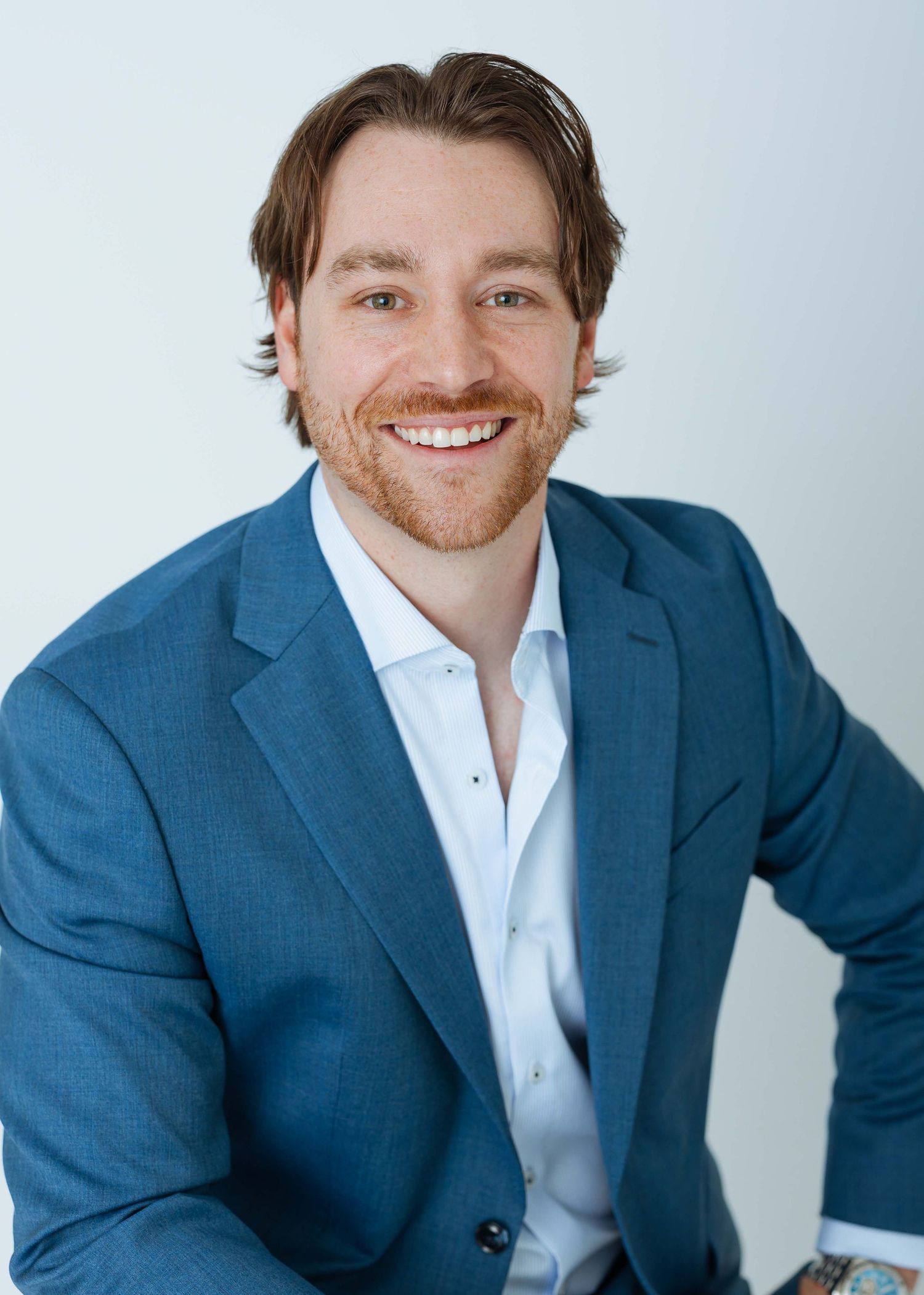 Smiling man with beard wearing blue blazer and white shirt poses for professional headshot photo.