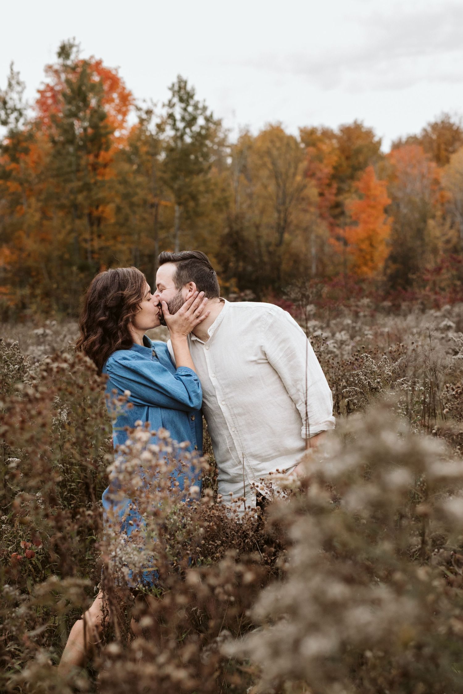 A couple shares romantic moments among wild grass during autumn sunset.