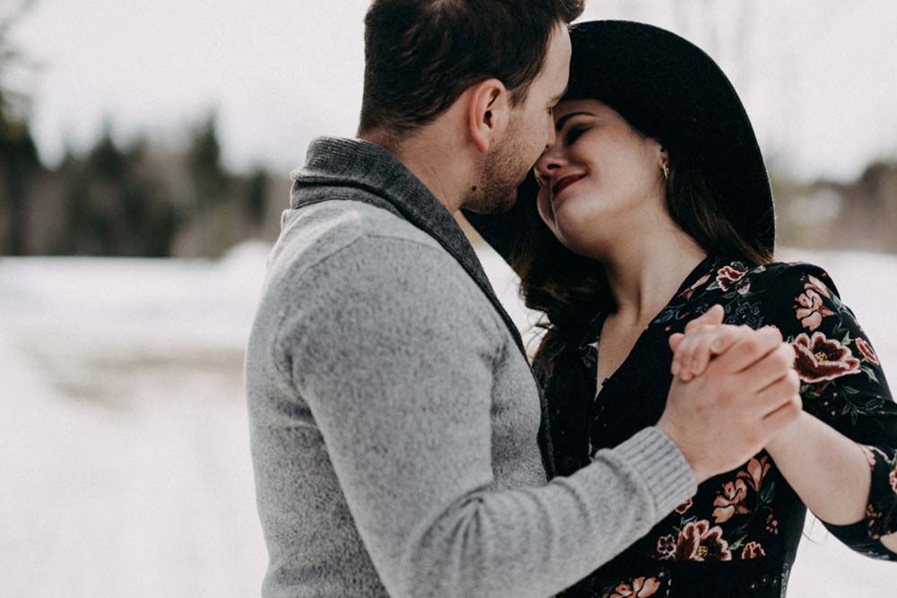 Romantic winter engagement photo of a couple in warm clothing sharing a close moment.