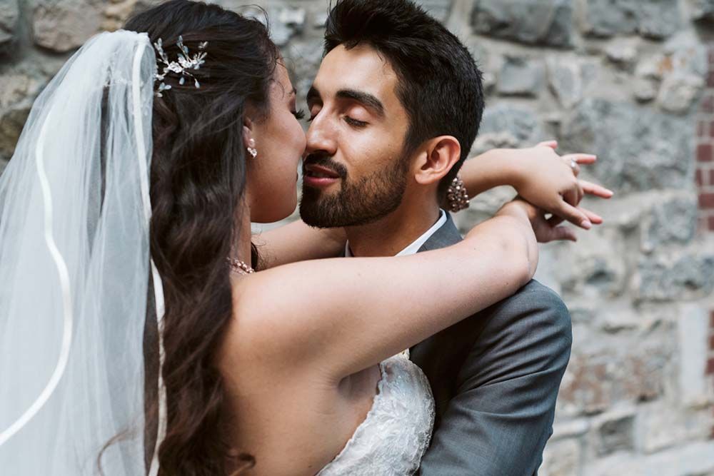 Intimate wedding moment captured in black and white against stone wall.