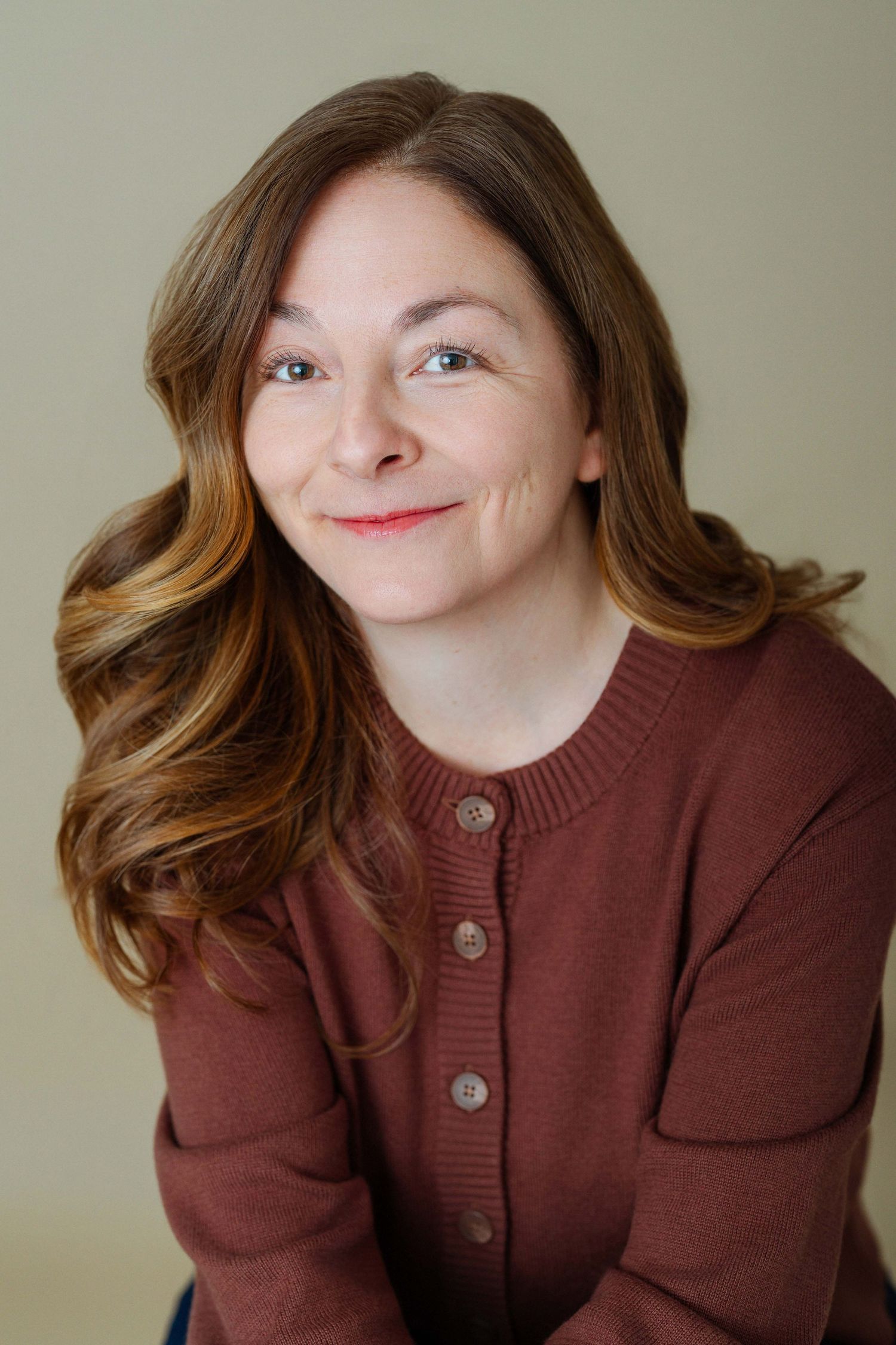 Smiling woman with auburn hair wearing a burgundy cardigan poses for a professional headshot photo.