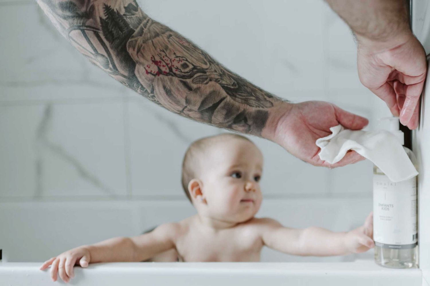 Baby lying on white sheets receiving gentle massage from adult hands.