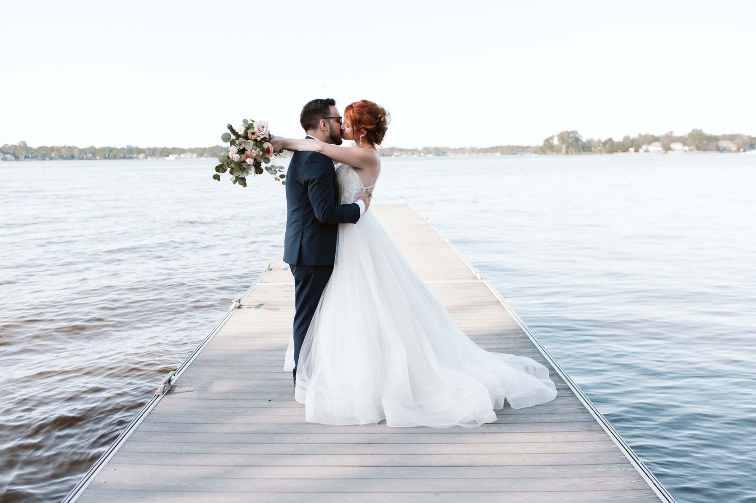 Romantic wedding portraits captured on a wooden dock by the water at sunset.