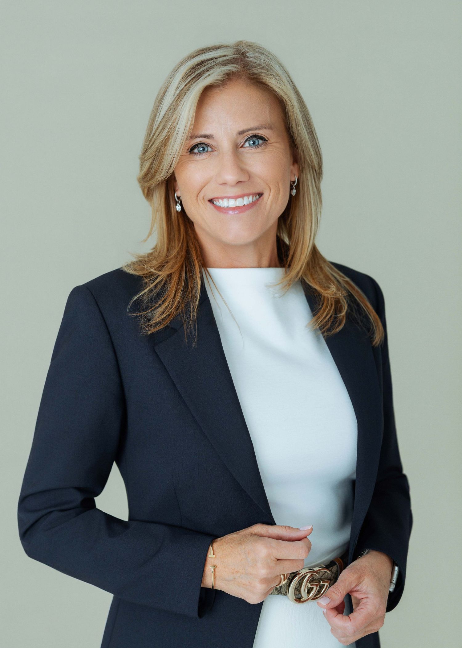 Professional woman in navy blazer and white top smiling confidently against a neutral background.