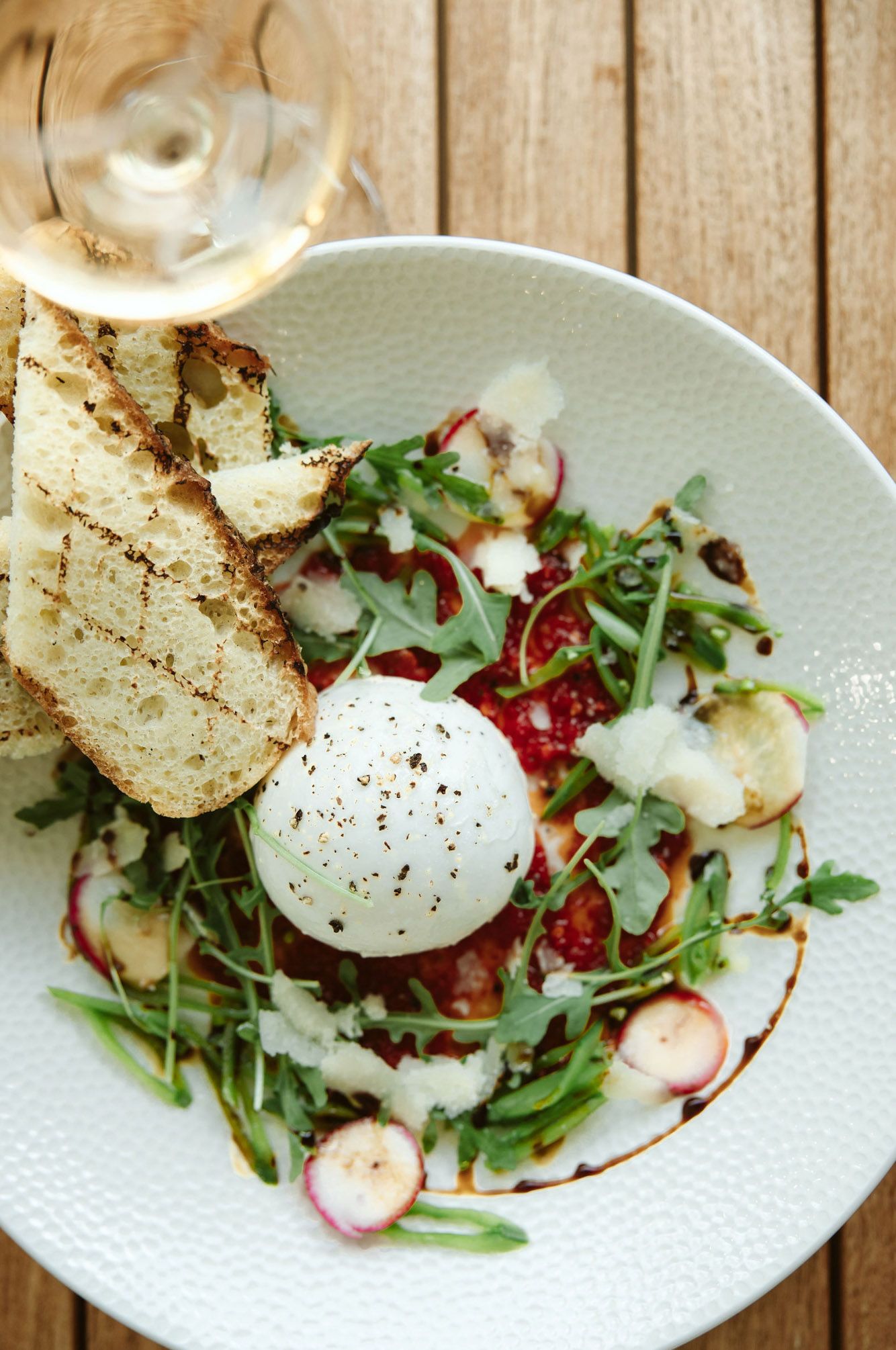 Elegant salad with poached egg, radishes, and microgreens on textured white plate.