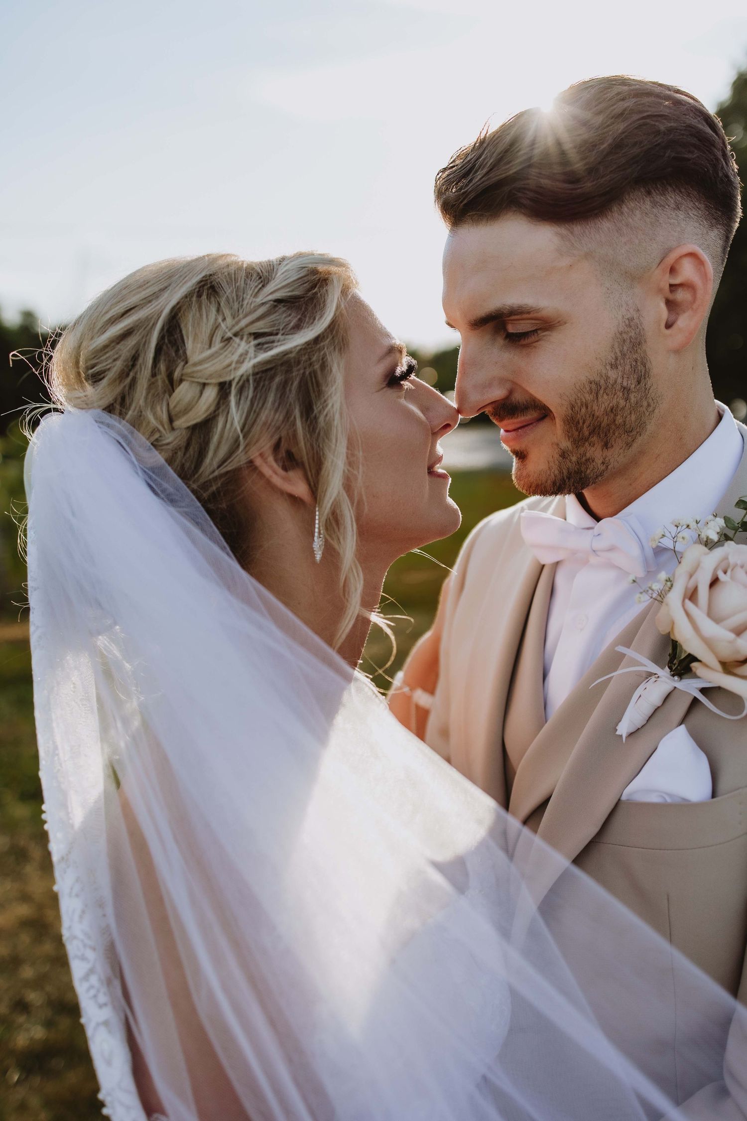 Intimate close-up of a couple sharing a romantic moment in golden sunlight with flowing veil.