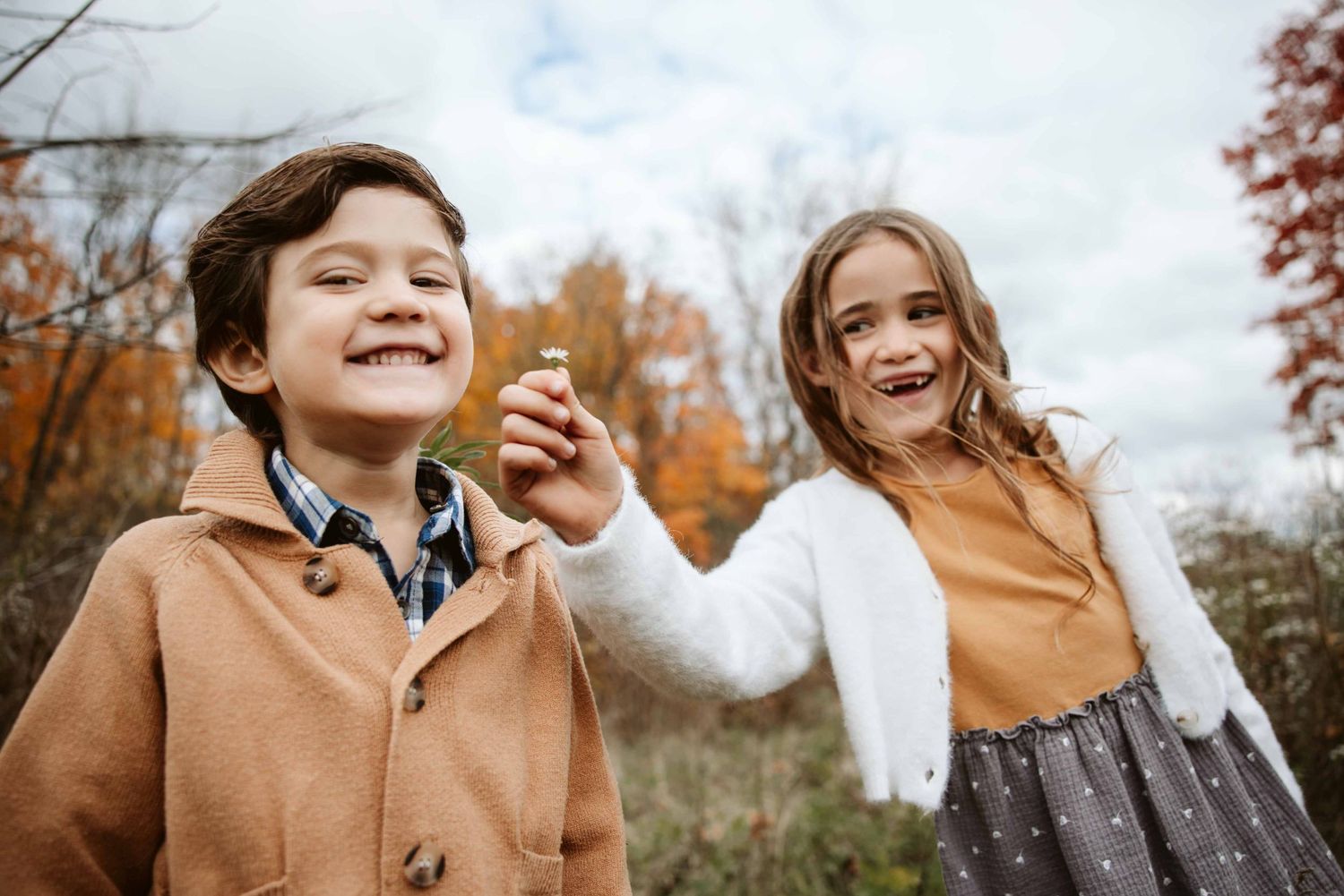 Two children laughing and holding hands during an autumn photoshoot.