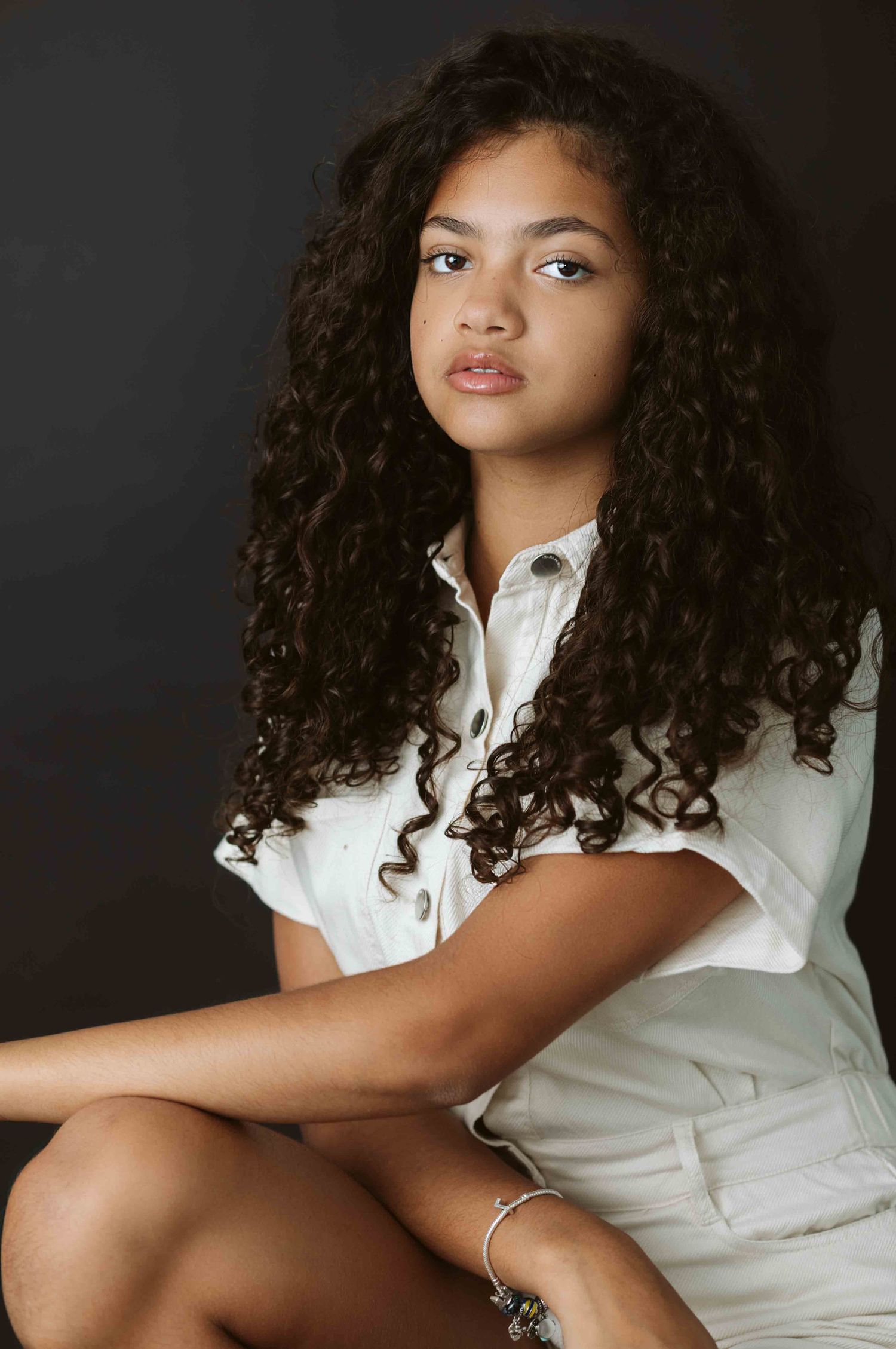 Portrait with curly hair in white button-down shirt against dark background.