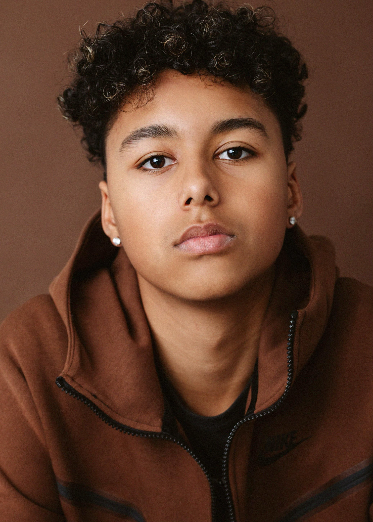 Portrait series featuring someone in a brown hoodie against a warm brown background.