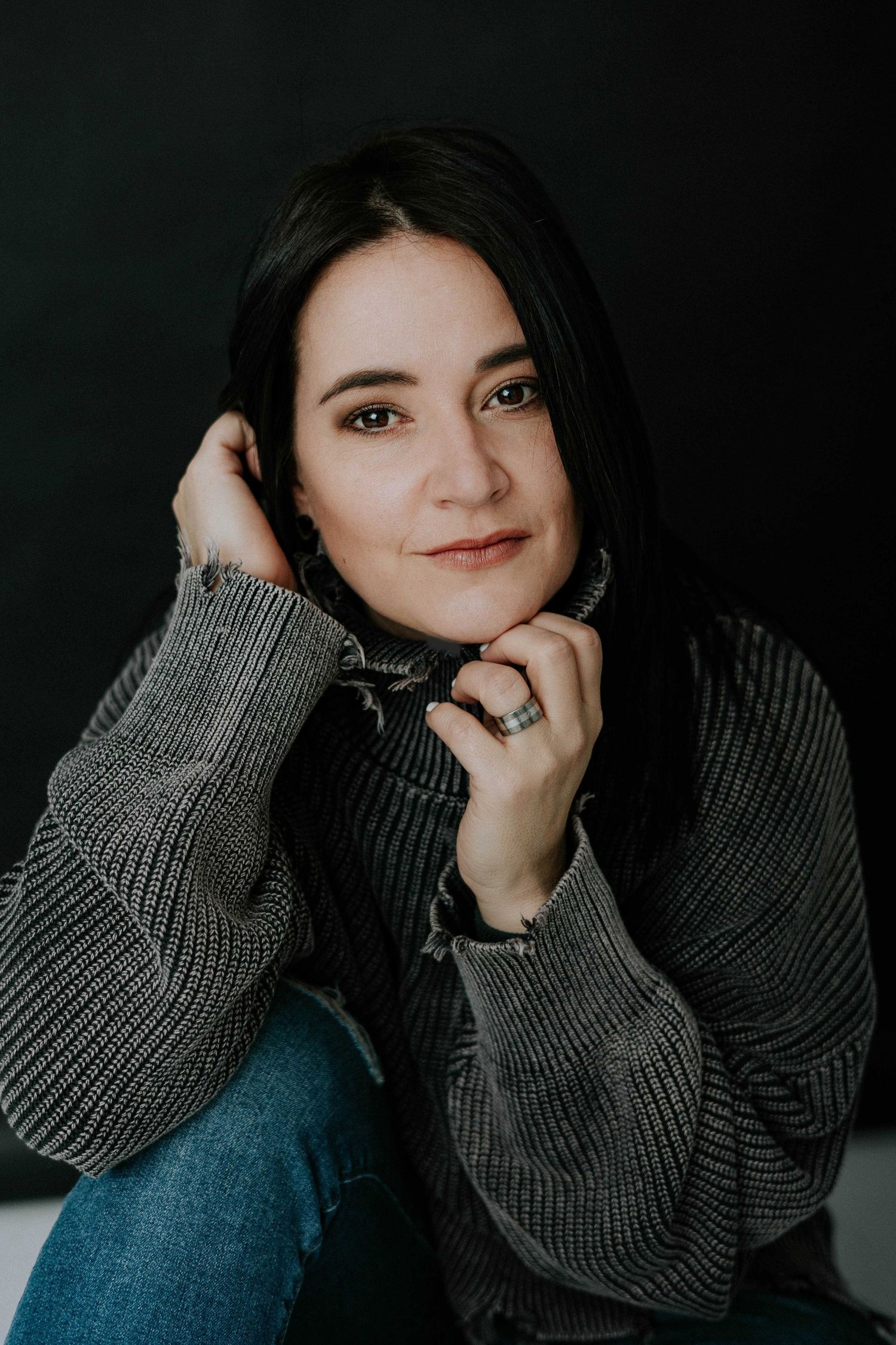 Moody portraits in grey sweater against dark background with dramatic lighting.