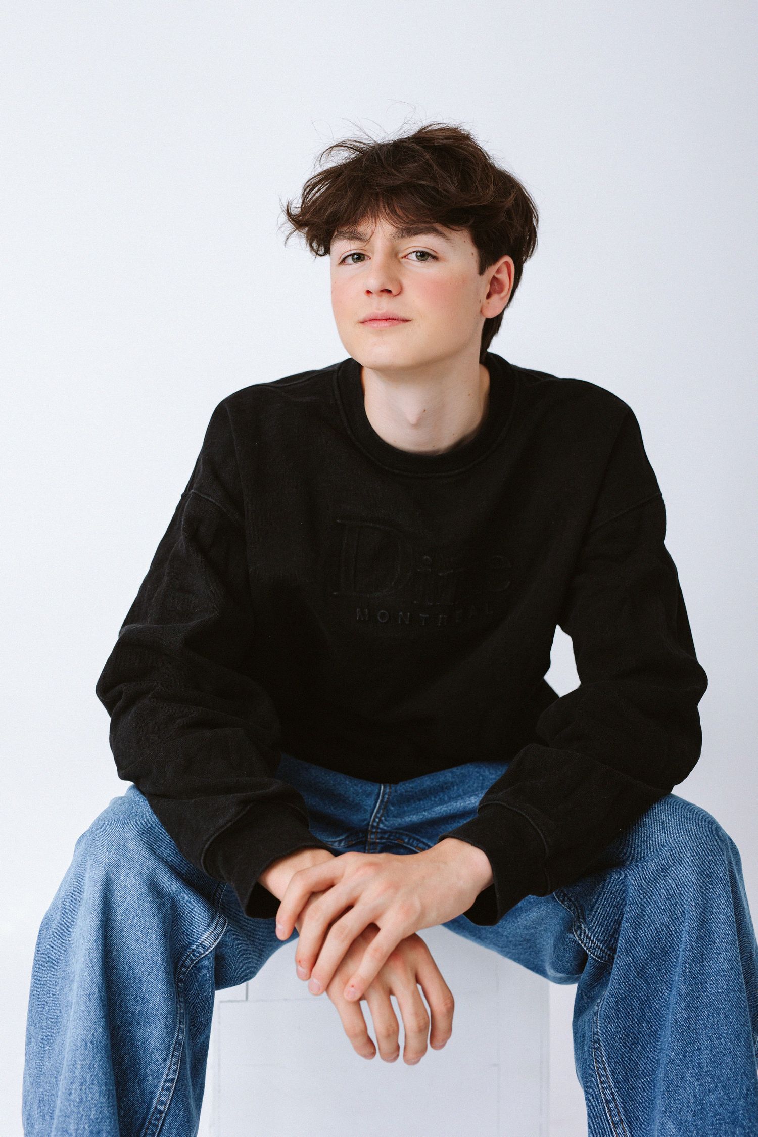 Person in black sweater and jeans poses casually against white studio background.