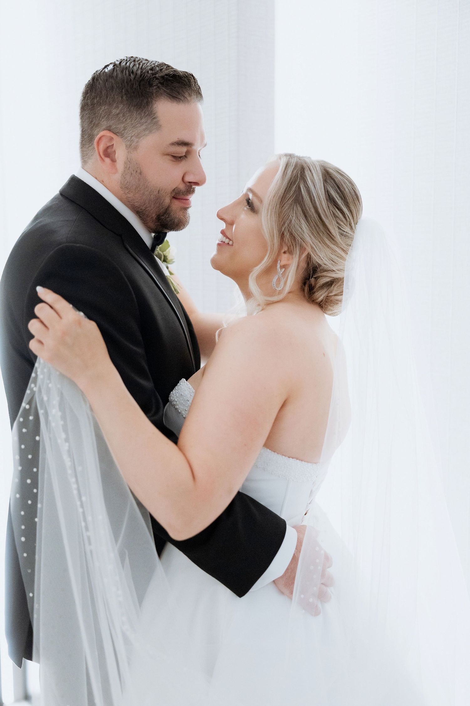 Romantic wedding portrait showing couple embracing in white dress and black suit.