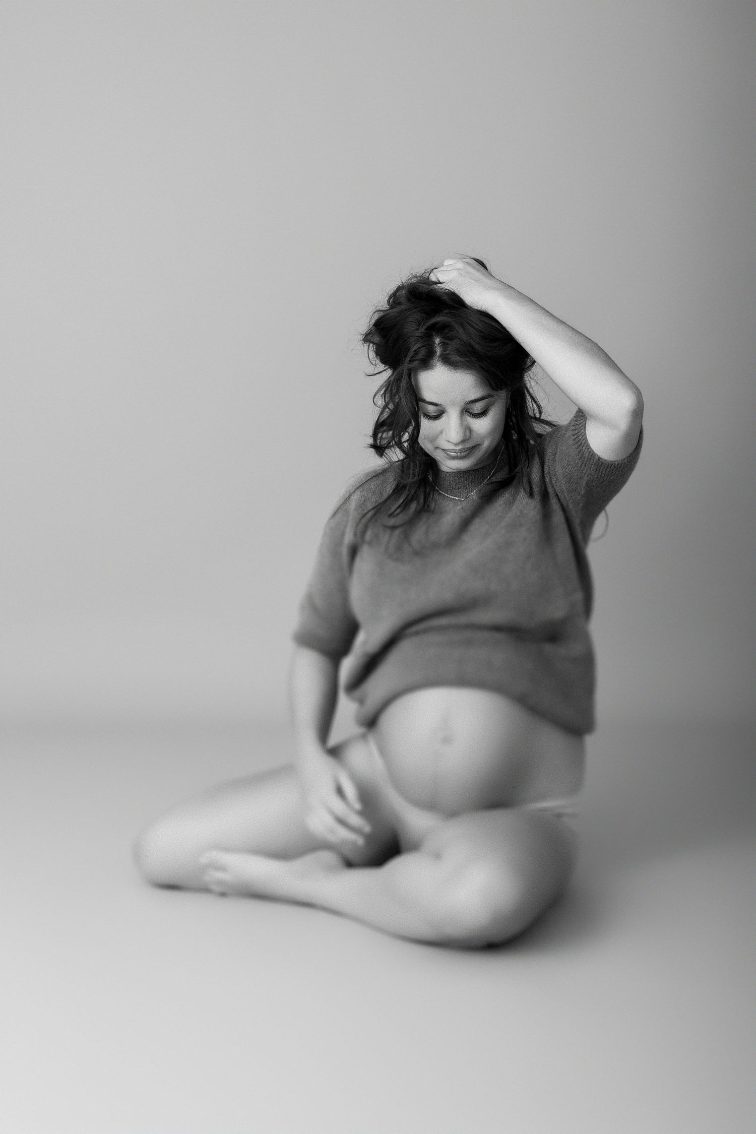 Intimate black and white maternity portrait showing pregnant belly in casual pose.