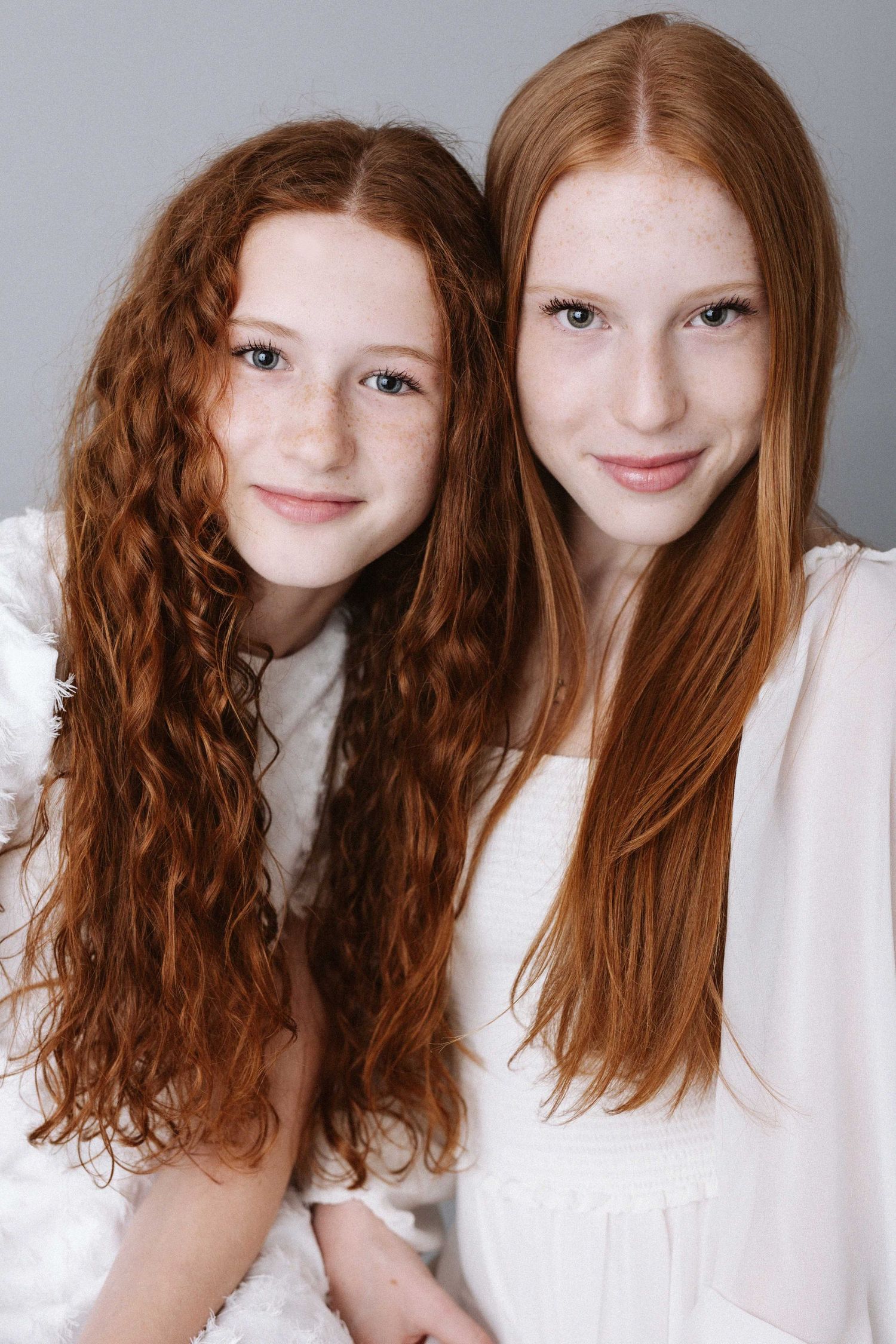 Two young people with long hair in white tops pose together in studio portrait series.