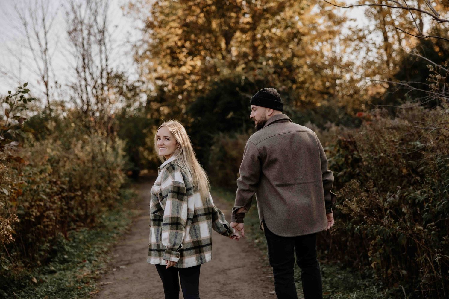 A couple holding hands while walking on an autumn path surrounded by fall foliage.