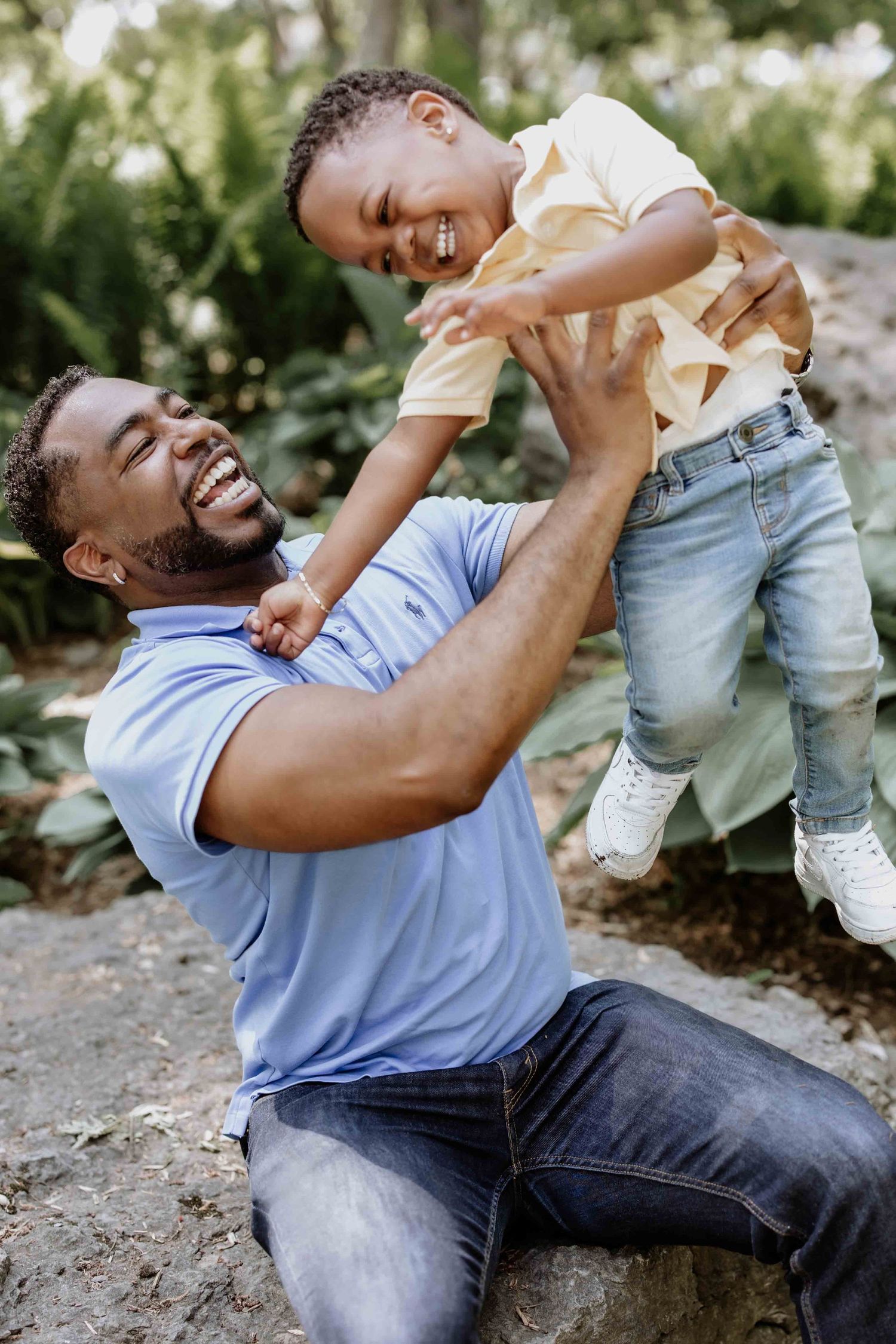Playful father lifting and playing with child outdoors in natural setting.