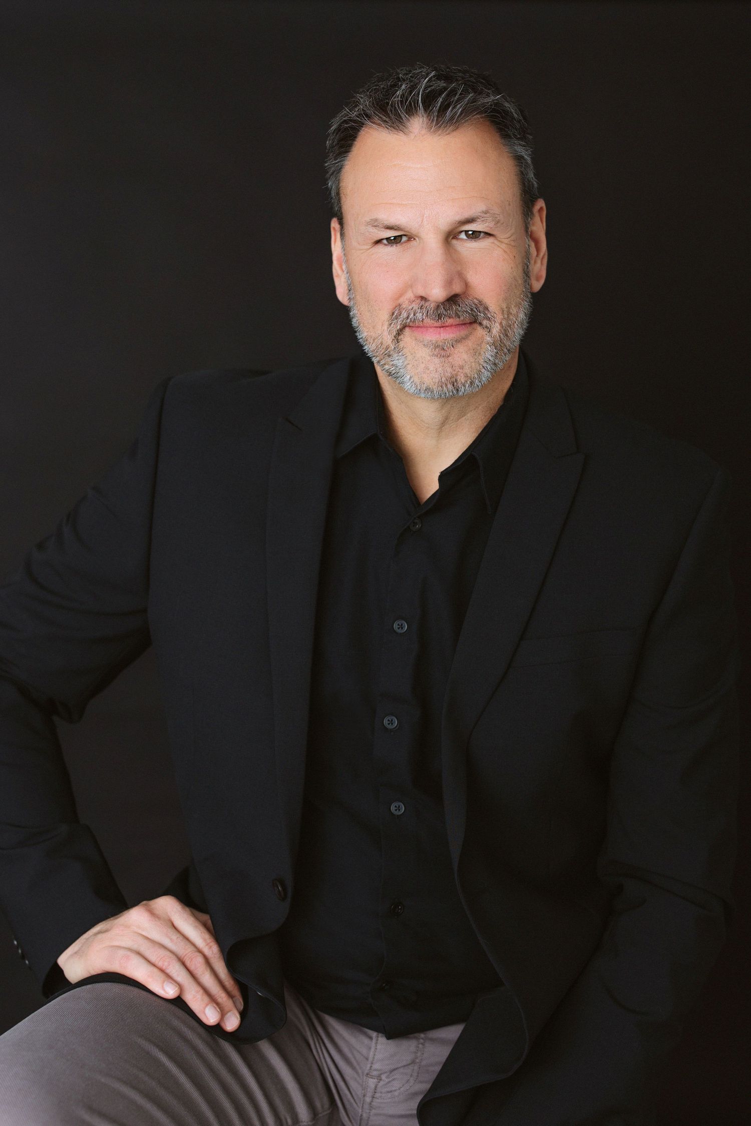 Professional studio portraits of man in black suit against dark background.