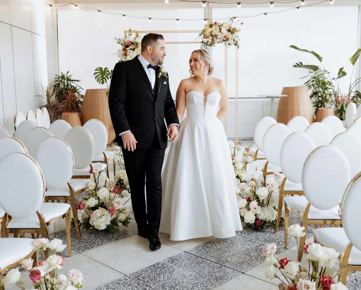 Modern white wedding reception space with elegant chairs and floral arrangements.