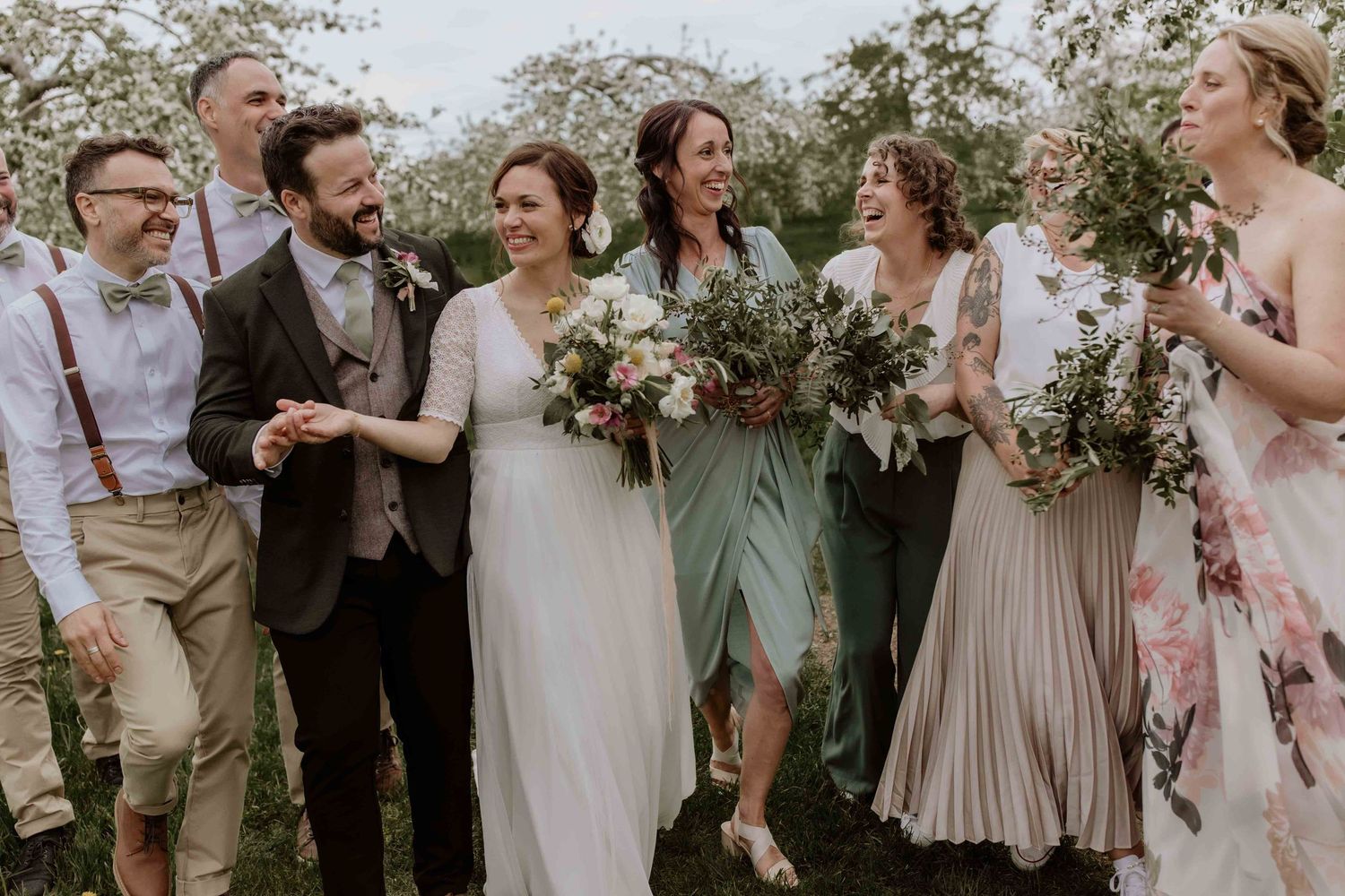 Wedding party poses outdoors in coordinated neutral tones with floral arrangements.