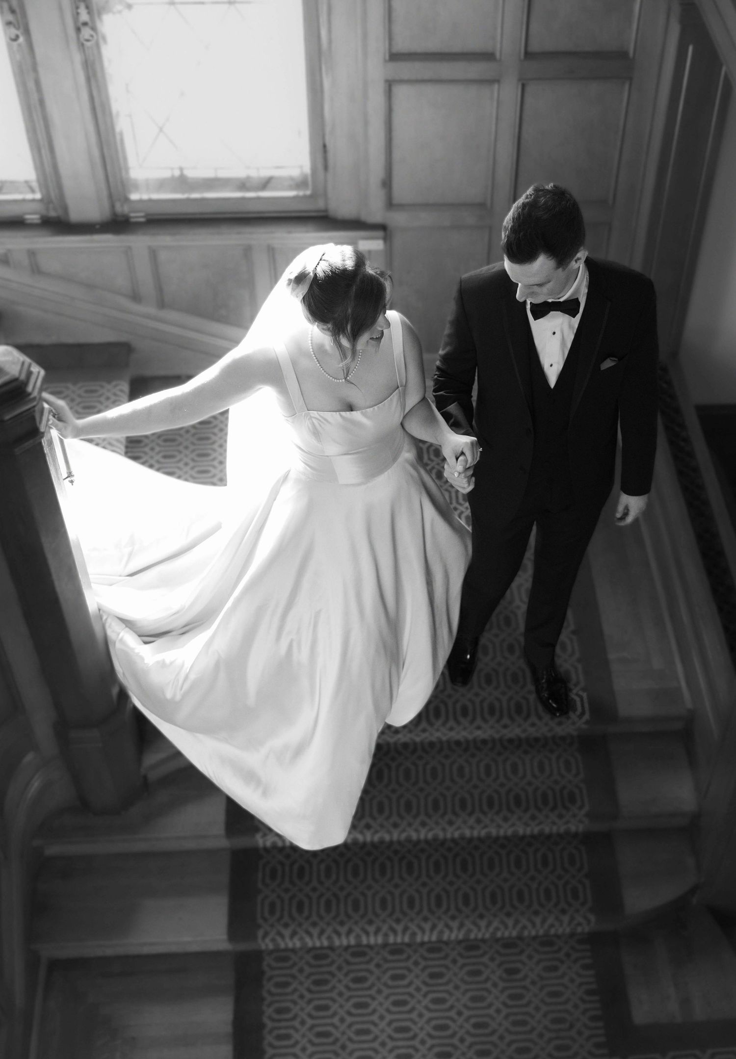 A sequence of black and white photos showing a bride's dress flowing dramatically down stairs with a groom beside her.