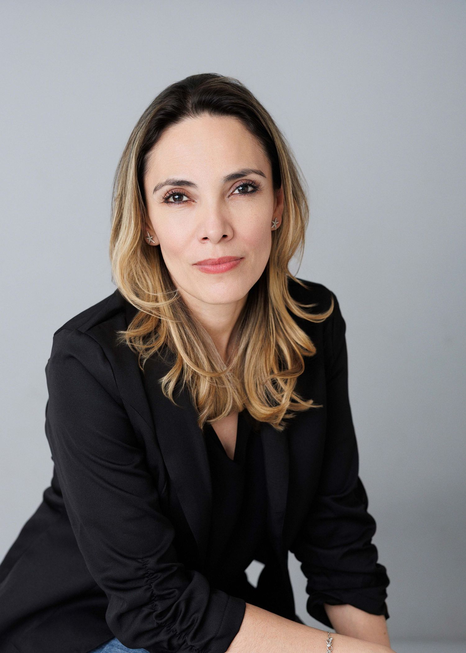 Professional headshot series showing someone in a black blazer against a gray background with varying poses and expressions.