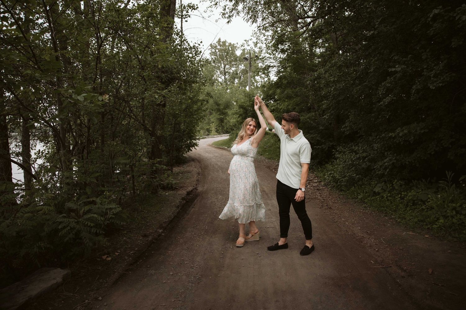 A couple dancing together on a tree-lined dirt path during a romantic photoshoot.