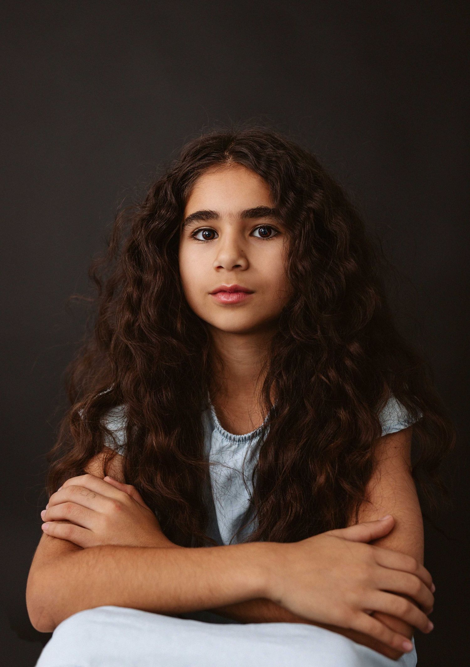 Studio portrait series showing a young person with long dark curly hair in a white top against a dark background.