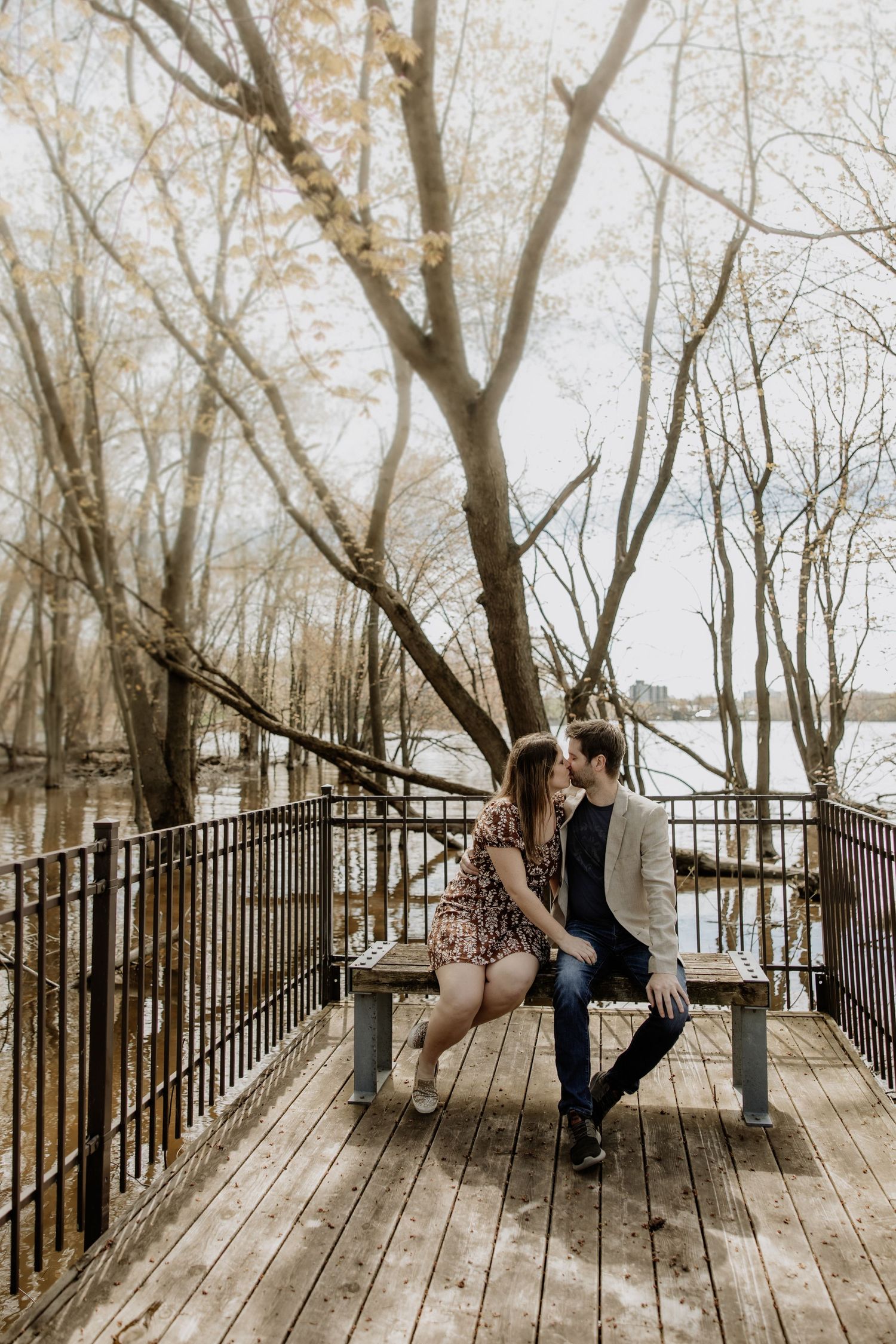 Romantic engagement photos on wooden boardwalk surrounded by bare winter trees.
