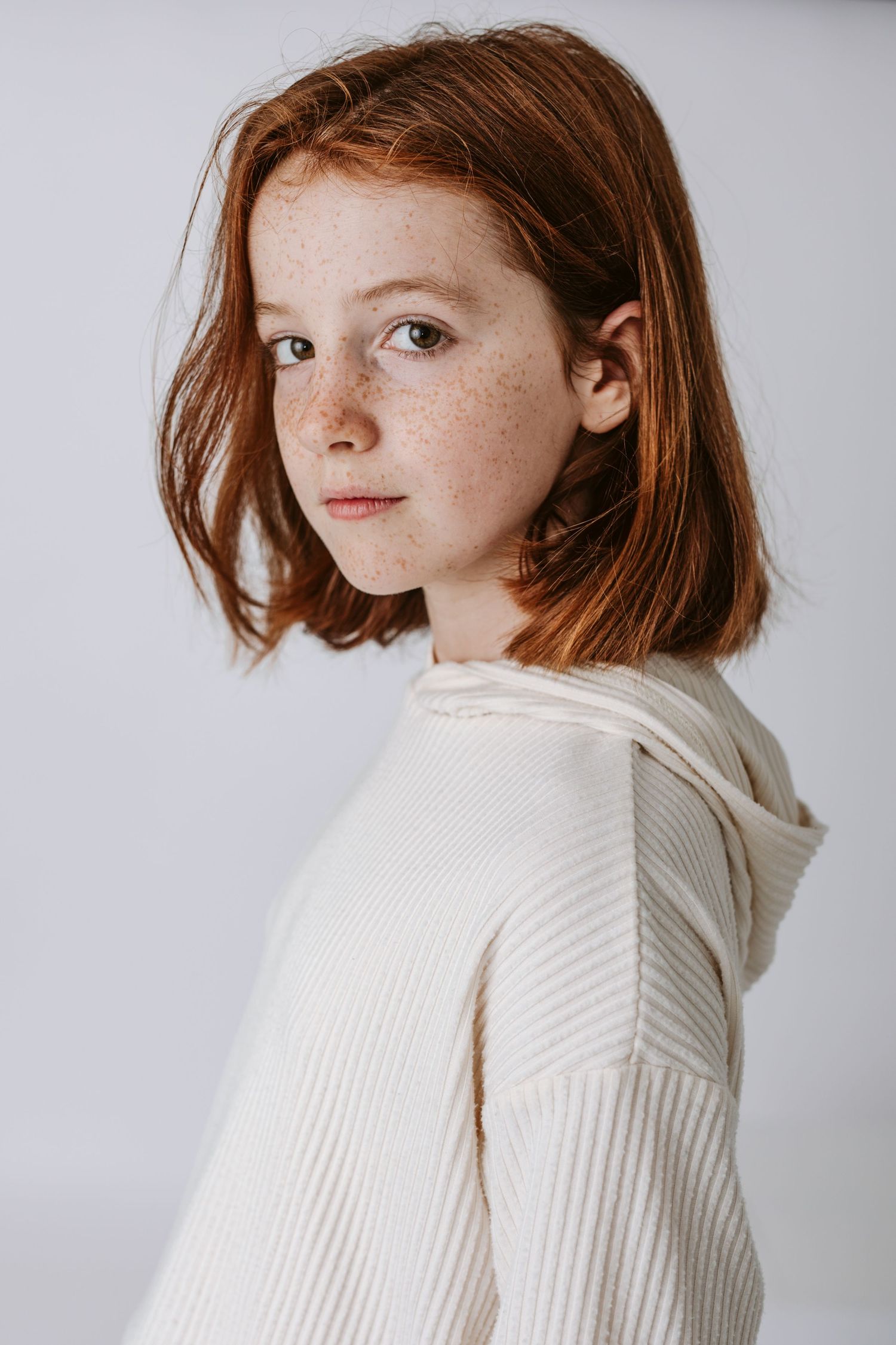 Person in cream turtleneck sweater poses in profile against white background.