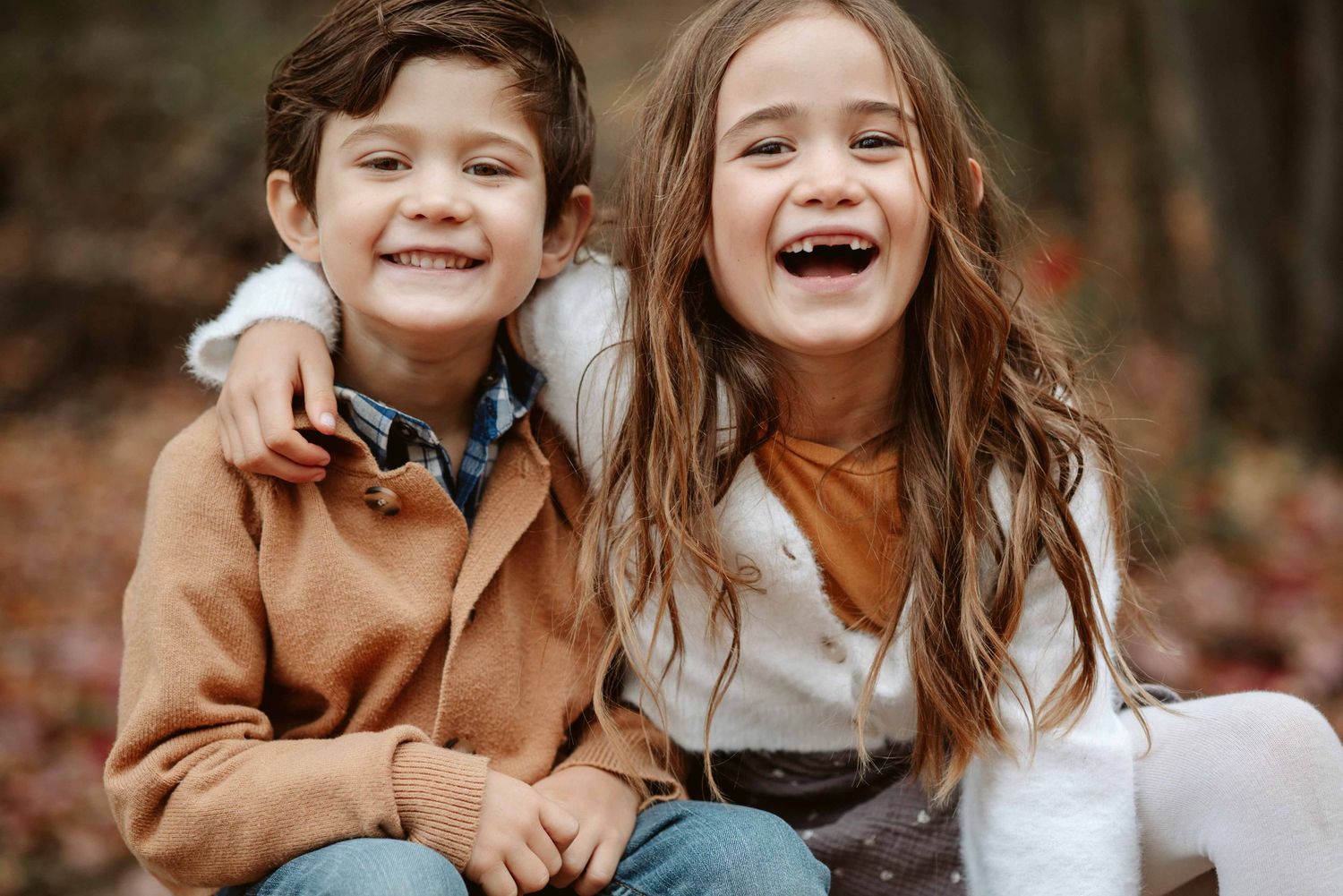 Two children sharing a joyful moment while sitting together outdoors.