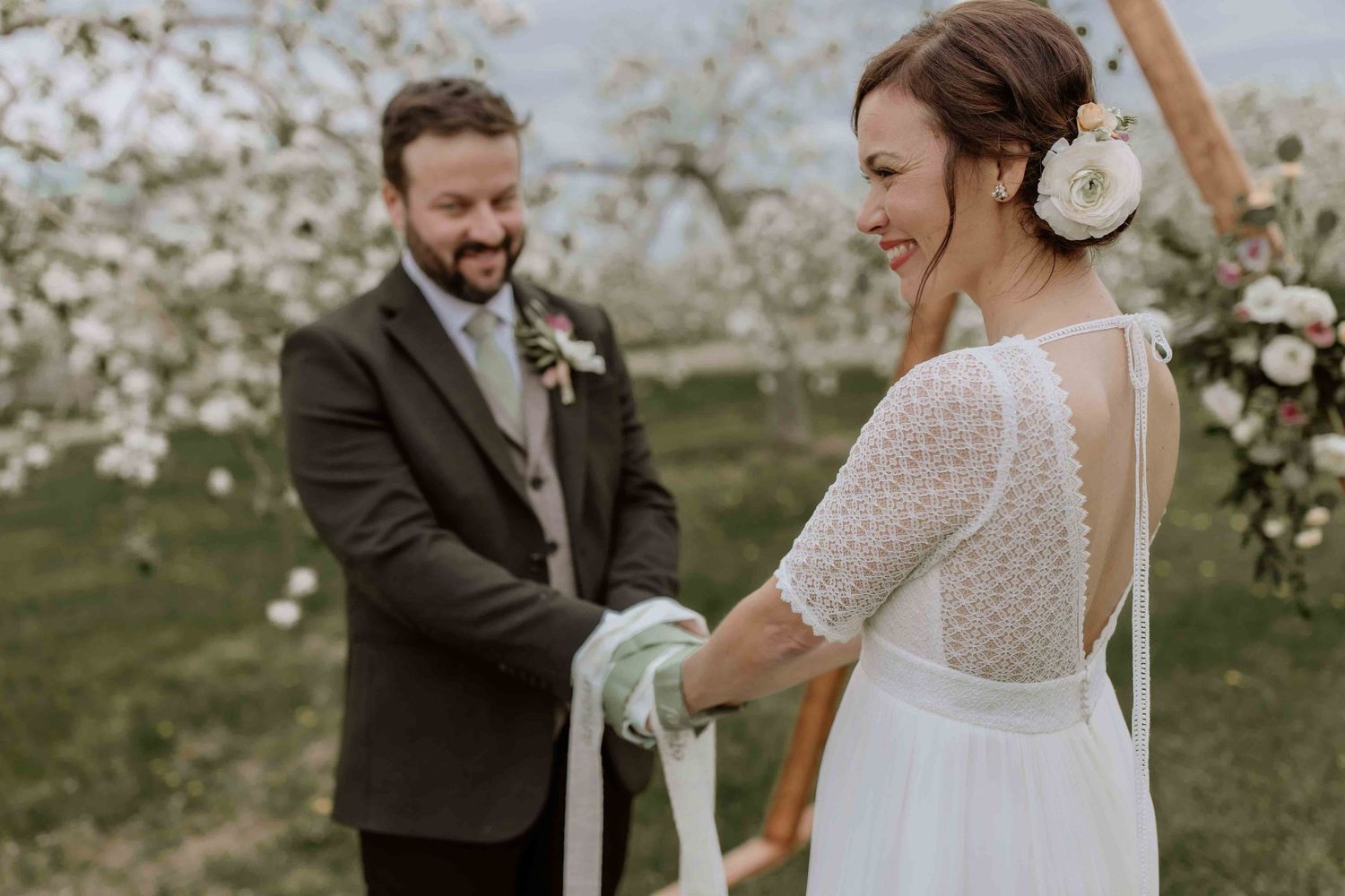 Wedding couple poses in blooming spring orchard during outdoor ceremony.