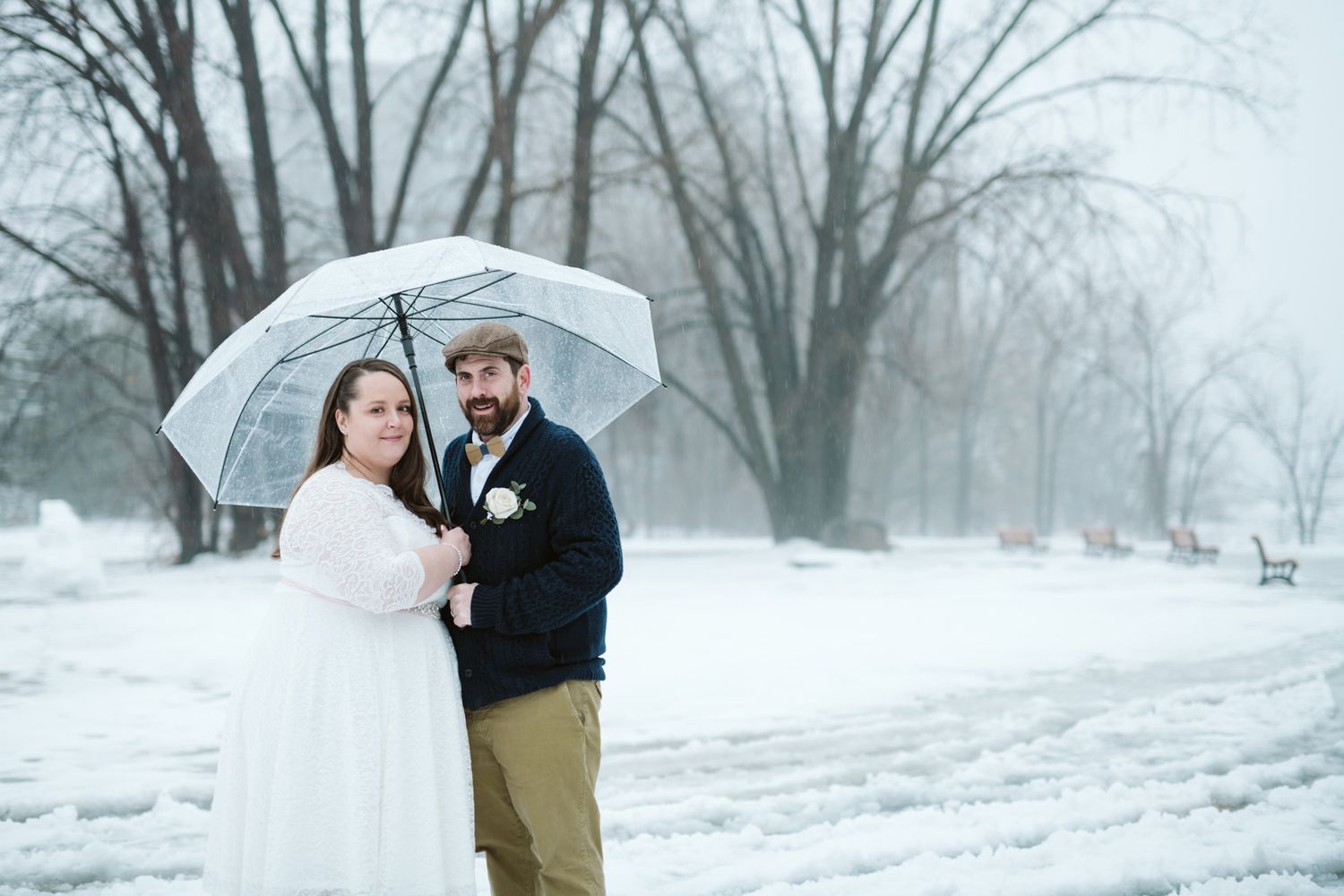 Winter wedding photos featuring a couple posing with white umbrellas in the snow.