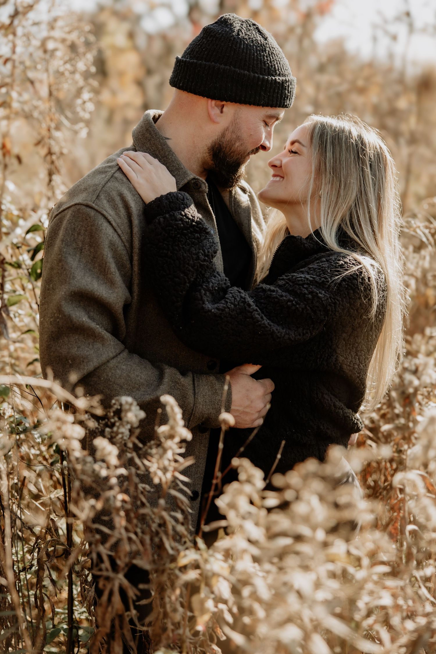 Romantic couple sharing intimate moments among tall dried grasses in autumn sunlight.