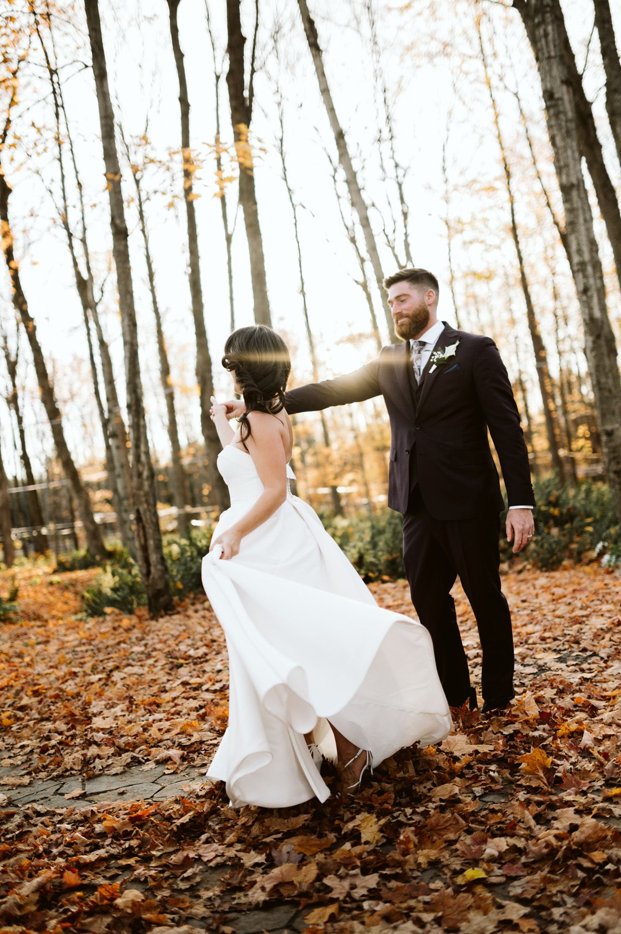 Wedding couple walks through autumn forest with fallen leaves.