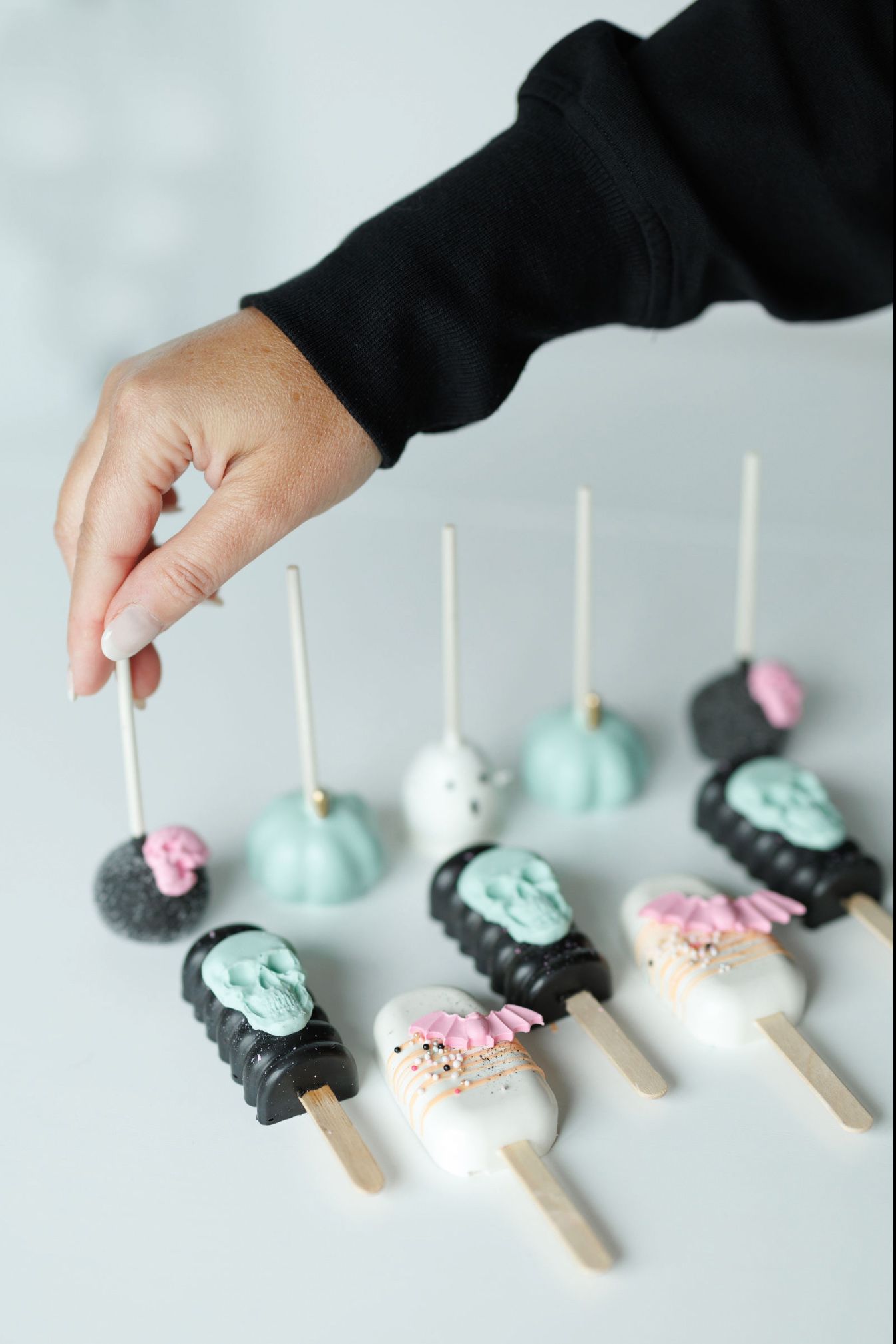 Colorful cake pops in pastel colors being arranged in a line against white background.
