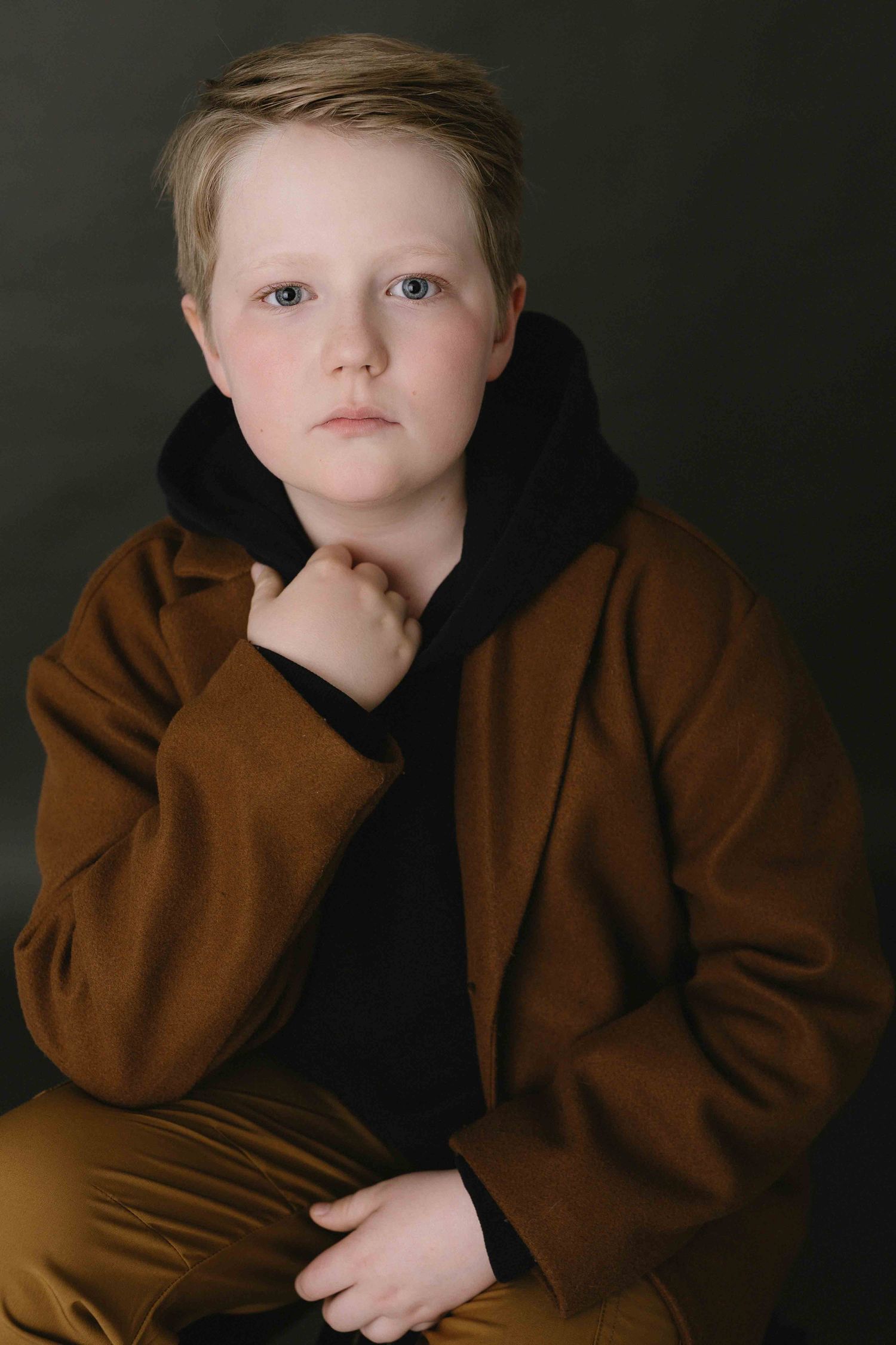 Studio portrait series featuring brown coat and thoughtful poses against dark background.