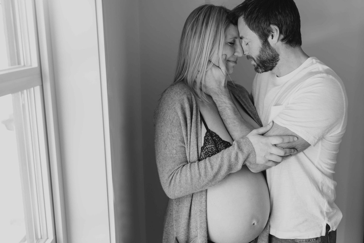 Intimate black and white maternity photo by window.