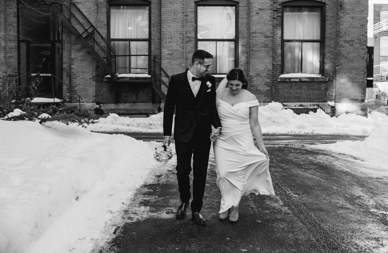 Winter wedding couple walks through snowy urban setting in black and white.