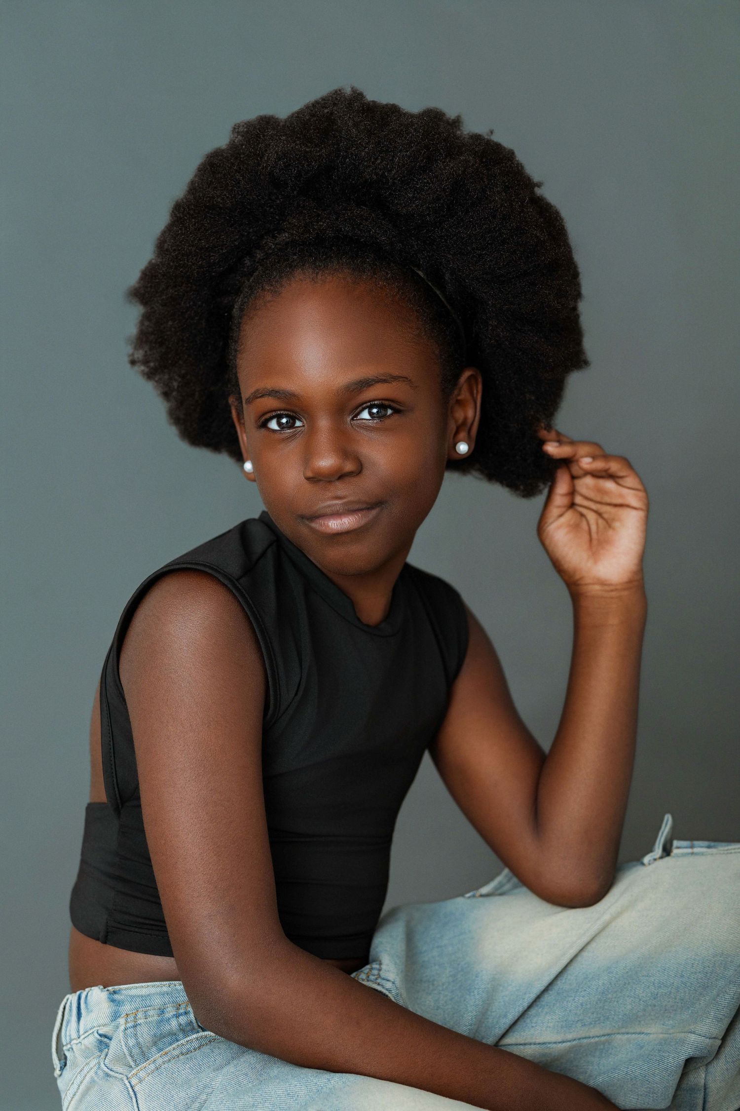 Young Black girl with natural afro hair wearing black crop top and jeans, posing confidently in studio portrait.