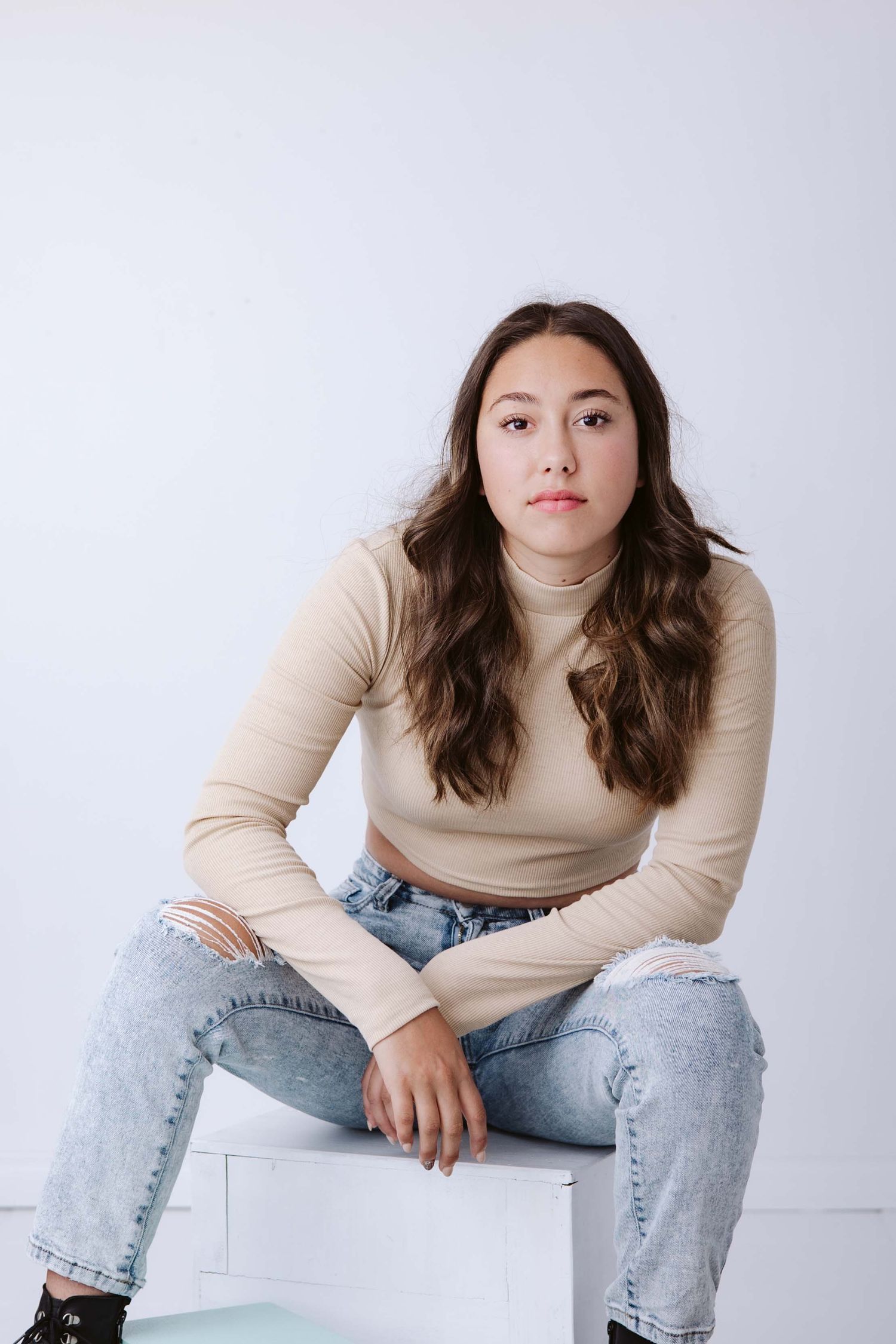 Casual portrait series in beige sweater and jeans sitting on white background.