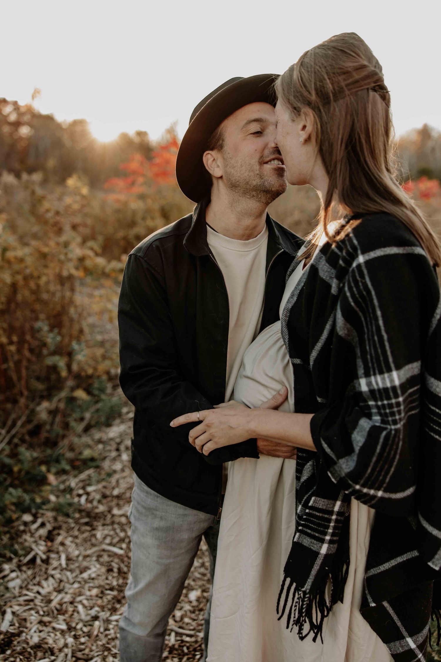 Romantic couple sharing an intimate moment at sunset in autumn with warm lighting and fall foliage in background.