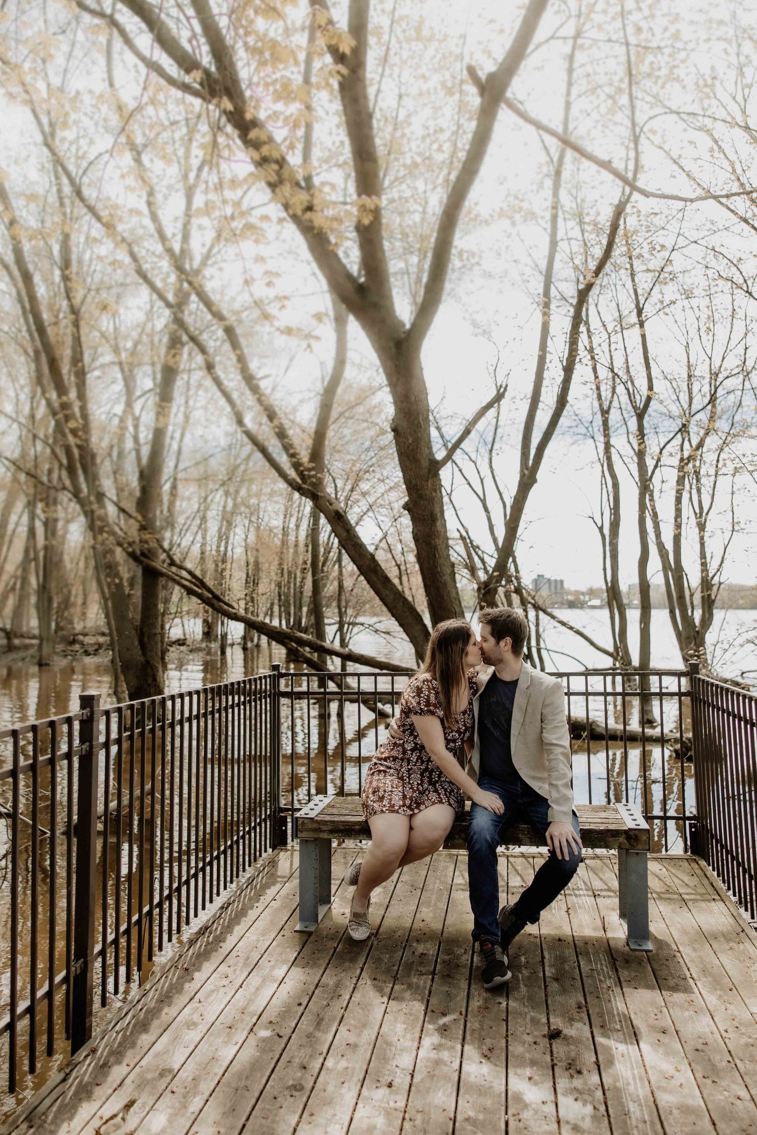 Couple sitting close together on bench during autumn boardwalk photoshoot.