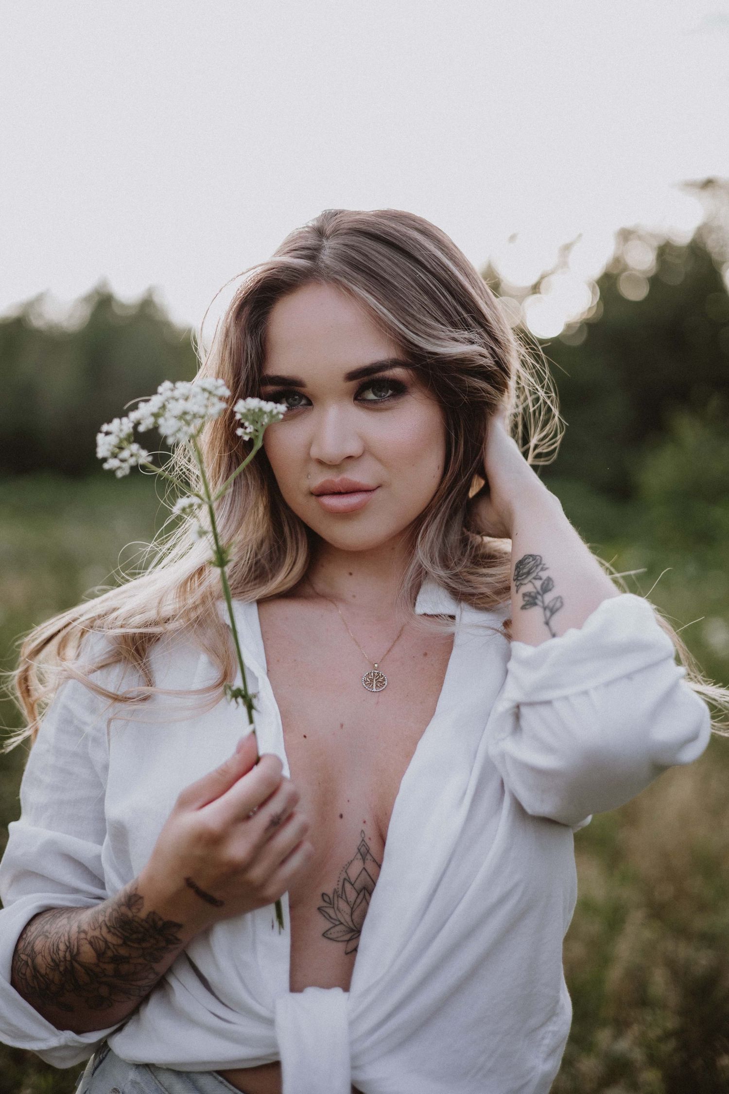 Portrait session in field with woman in white button-down shirt holding wildflowers.