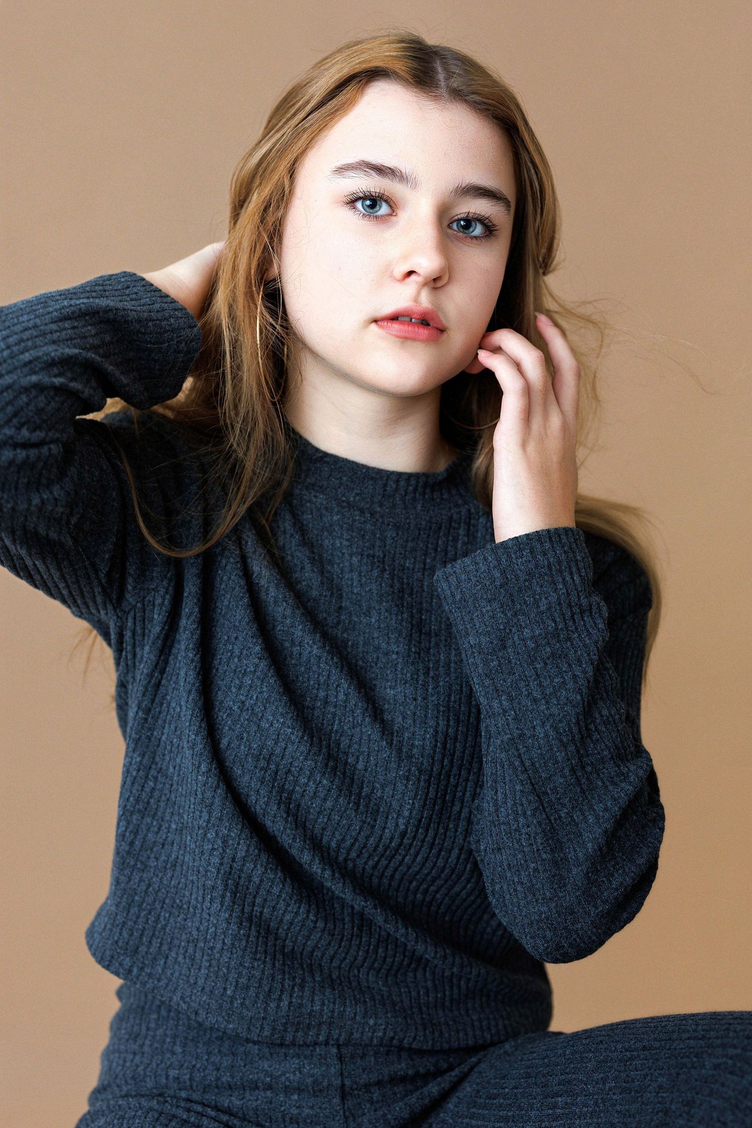 Fashion portrait series in dark sweater against warm neutral backdrop.