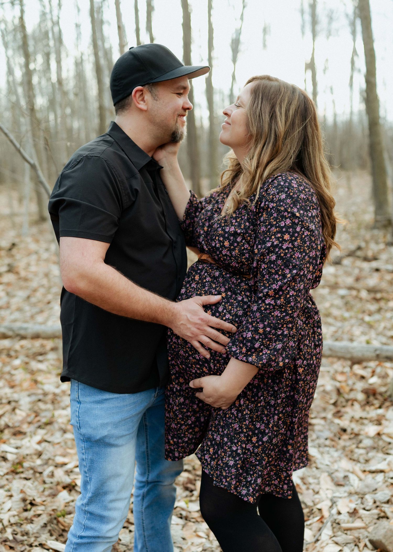 Expecting couple sharing a tender moment outdoors, man in black shirt and jeans with pregnant woman in floral dress.