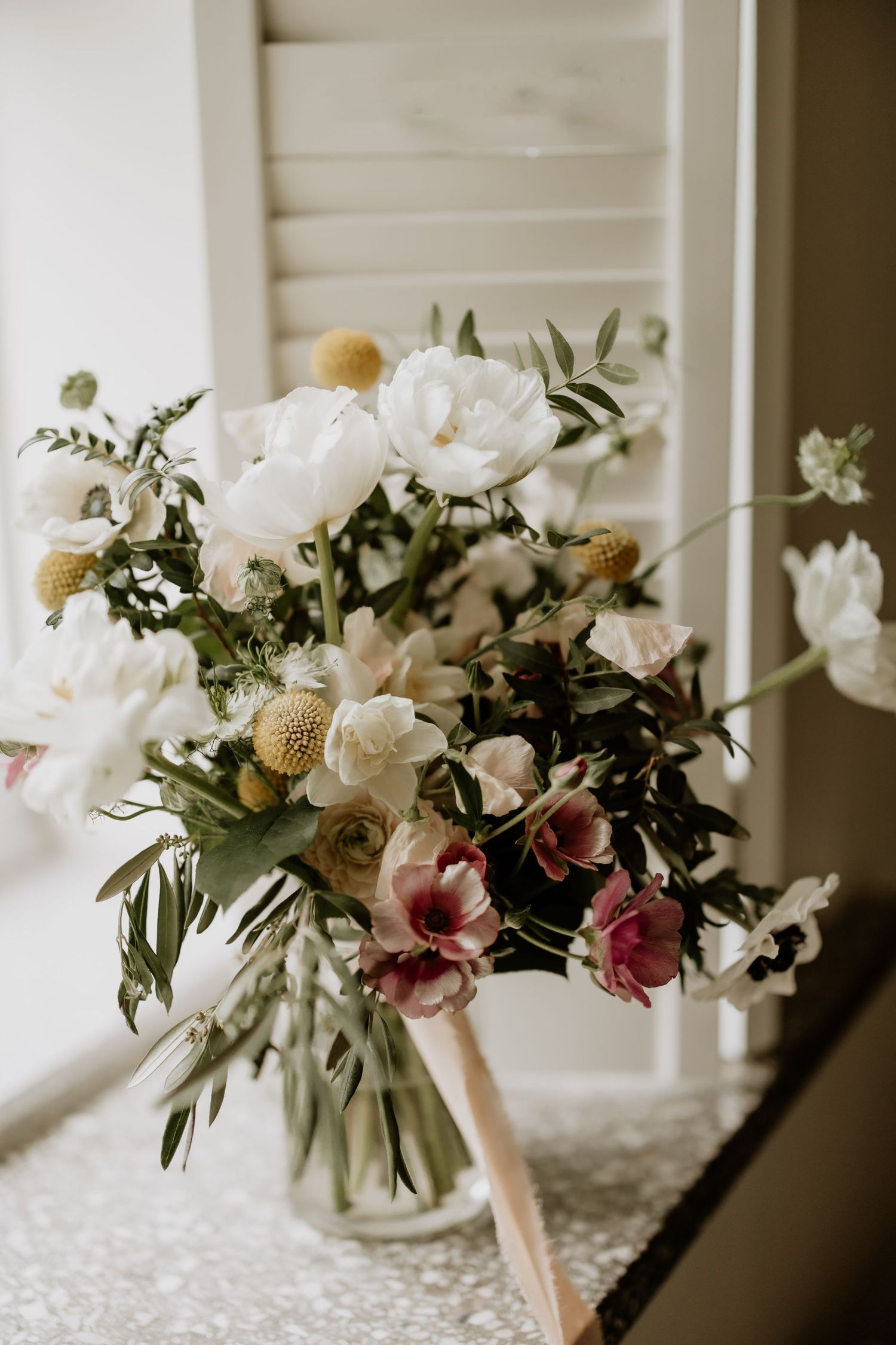 Elegant white and pink floral wedding centerpiece arrangement with greenery on textured surface.