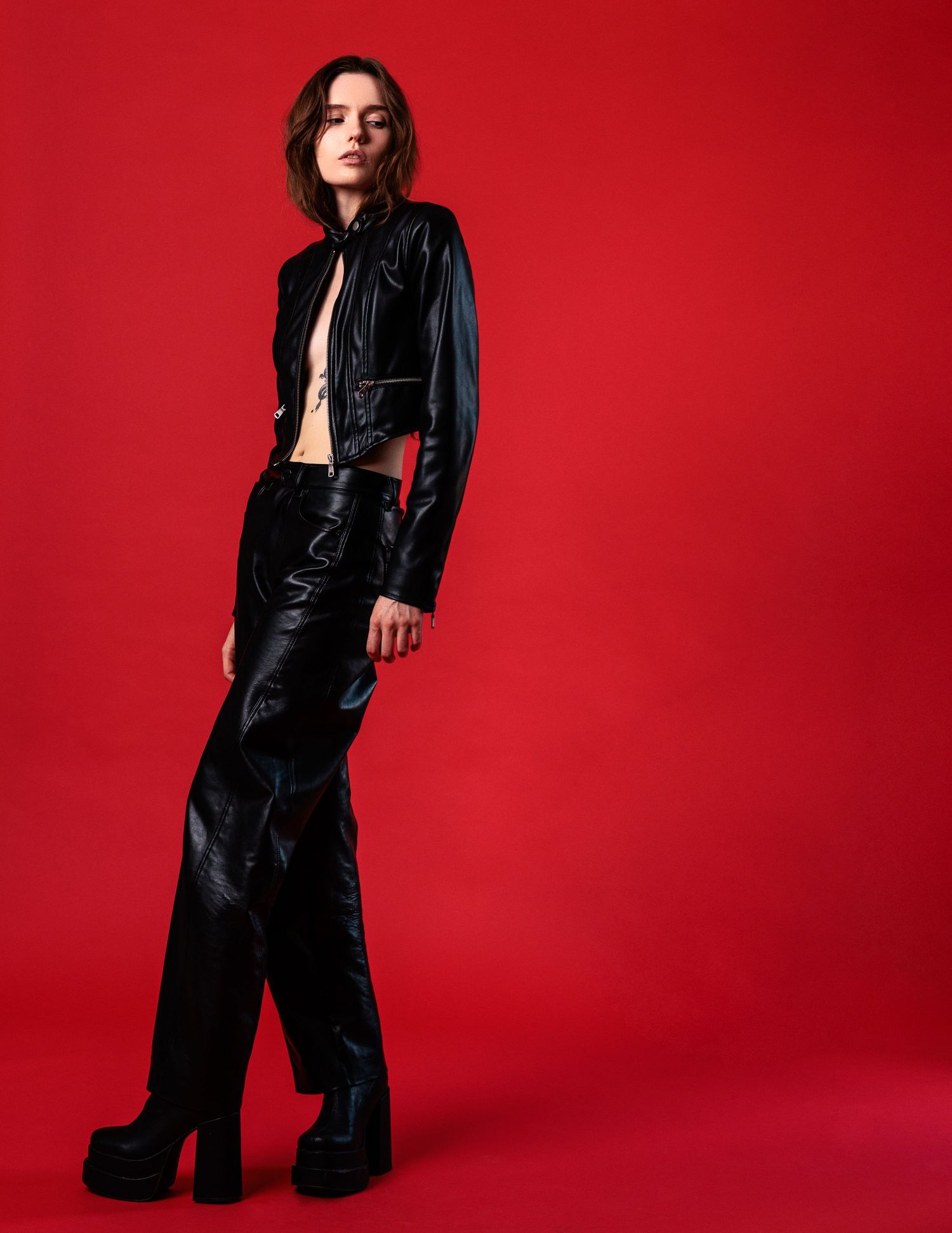 Black leather outfit styled against vibrant red backdrop in fashion editorial sequence.